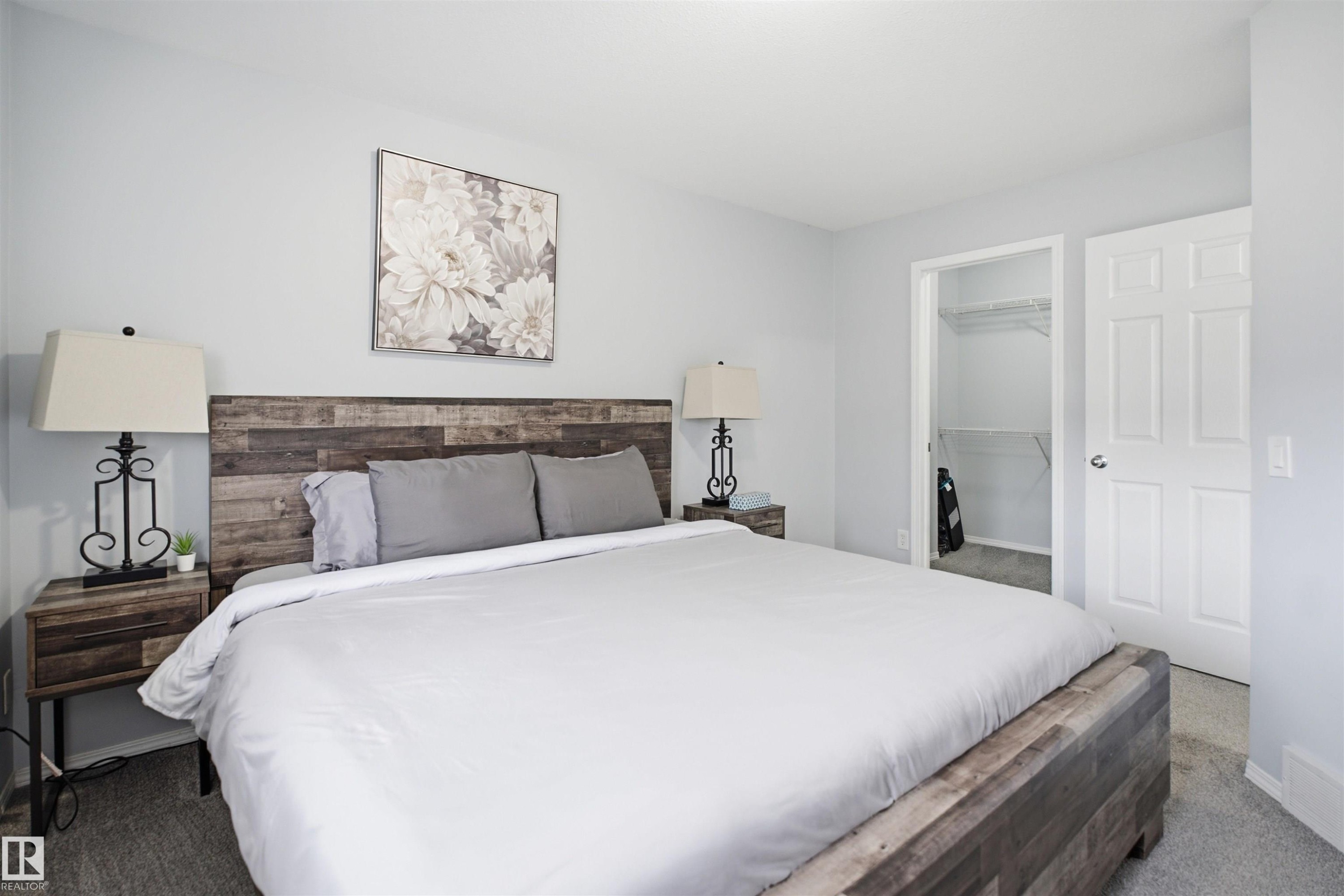 Bedroom featuring wood-finish flooring, light gray wall paint, and a built-in closet with shelving - 92 230 Edwards Drive, Edmonton, AB