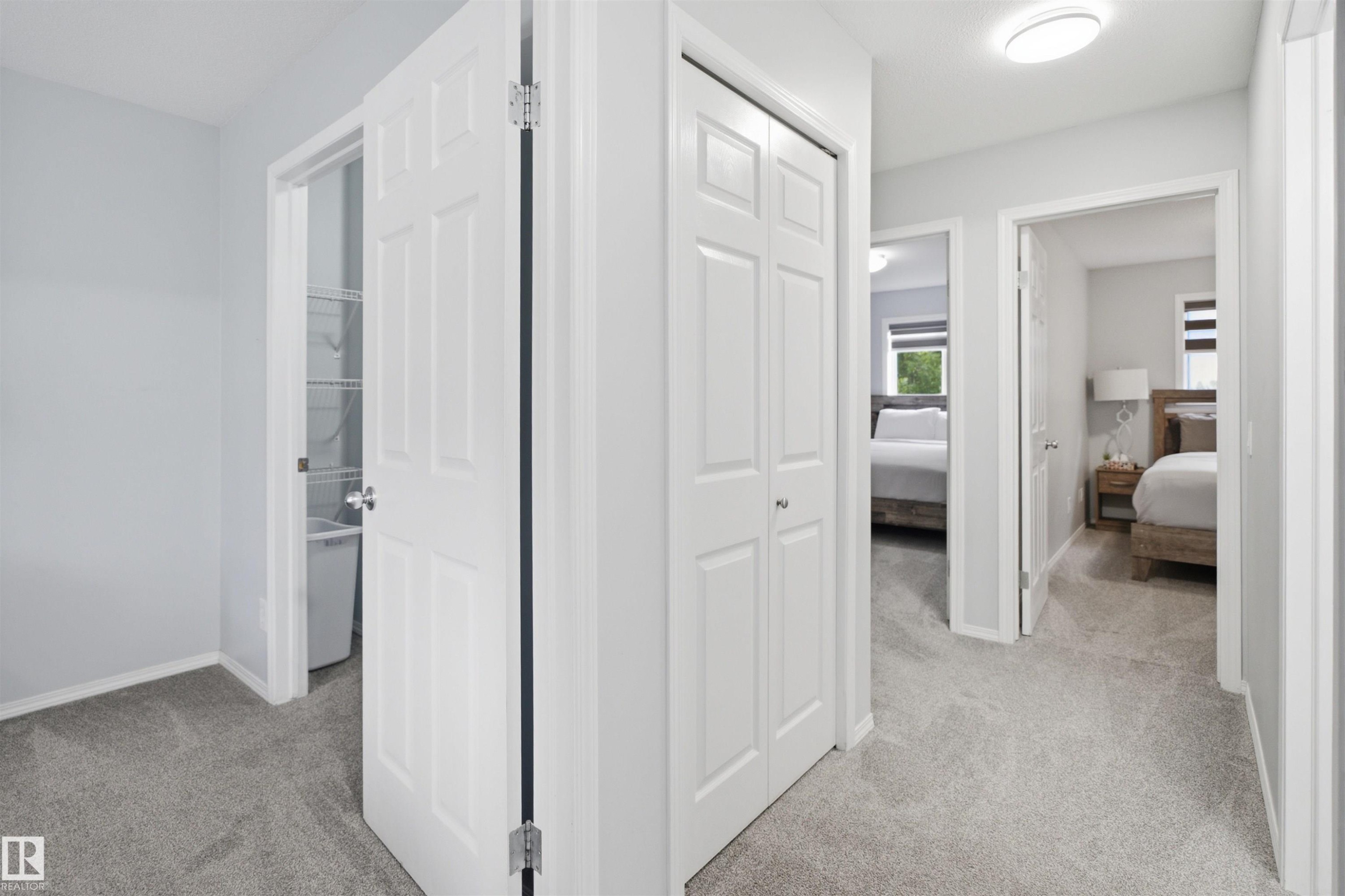 Carpeted hallway featuring white paneled doors, a flush-mount ceiling light, and built-in closet storage - 92 230 Edwards Drive, Edmonton, AB