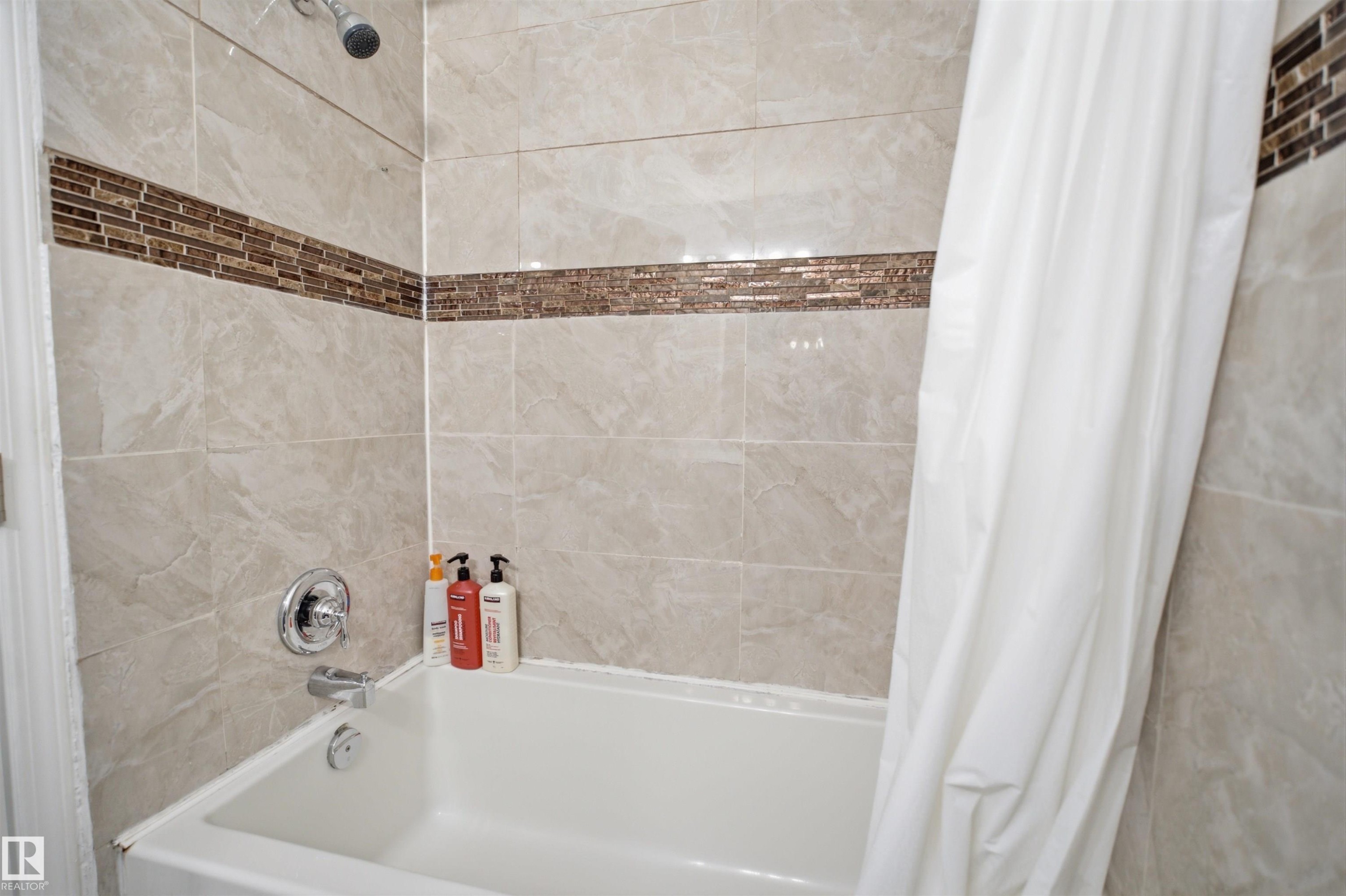 Bathtub with light-toned tiled surround and decorative mosaic accent band - 92 230 Edwards Drive, Edmonton, AB