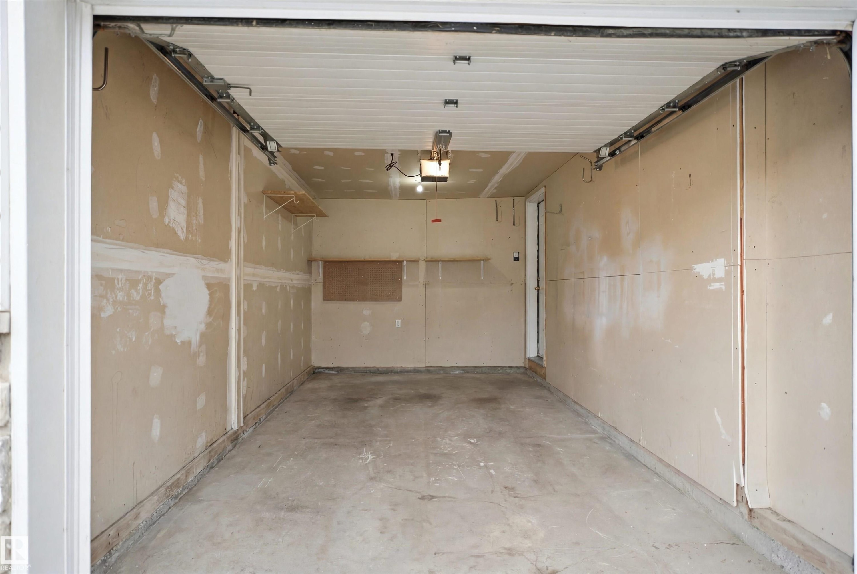 Interior garage space with concrete flooring, drywall-finished walls, an overhead garage door, and a built-in light fixture - 92 230 Edwards Drive, Edmonton, AB