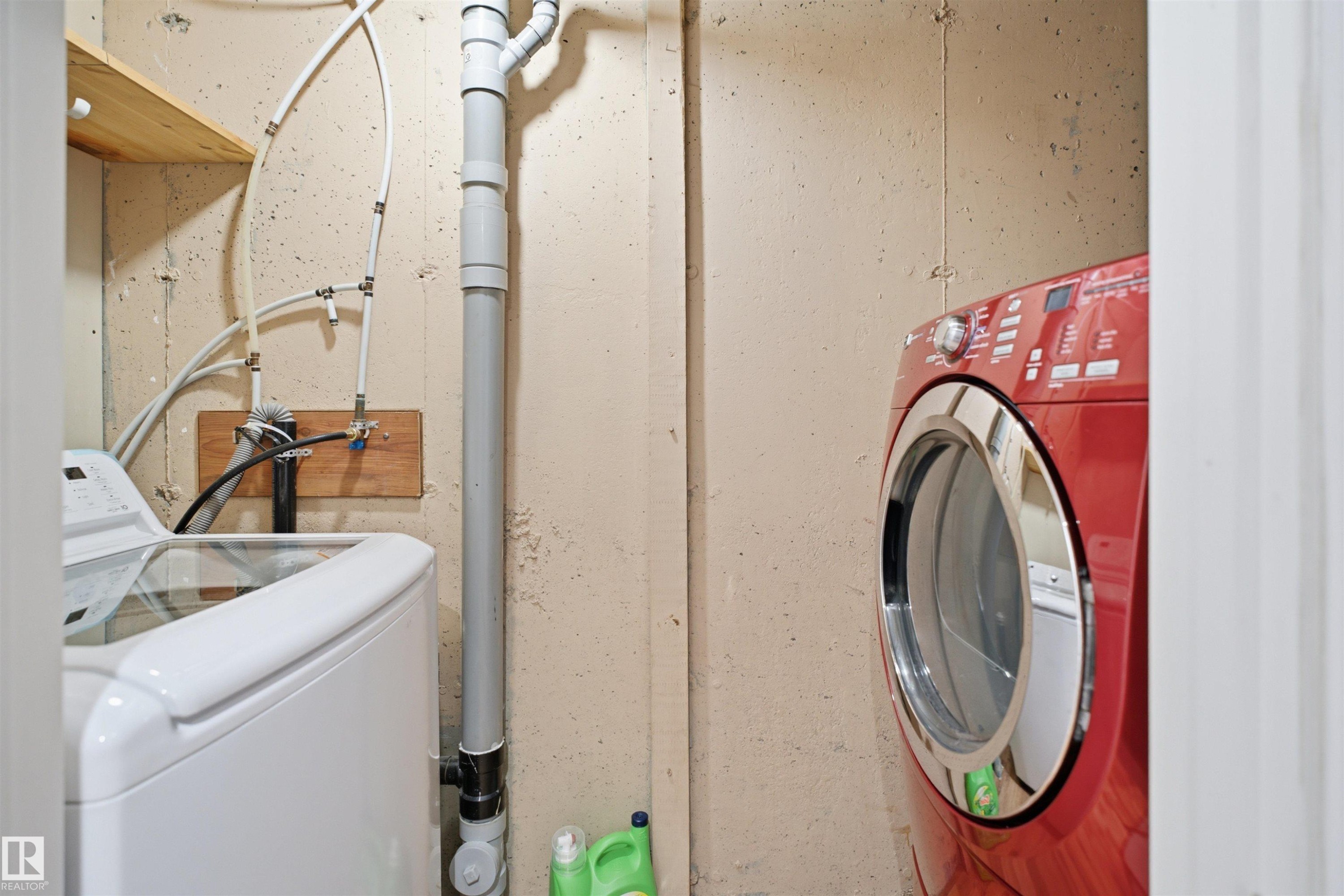 Laundry area with exposed concrete walls, visible plumbing, and wood shelving - 92 230 Edwards Drive, Edmonton, AB