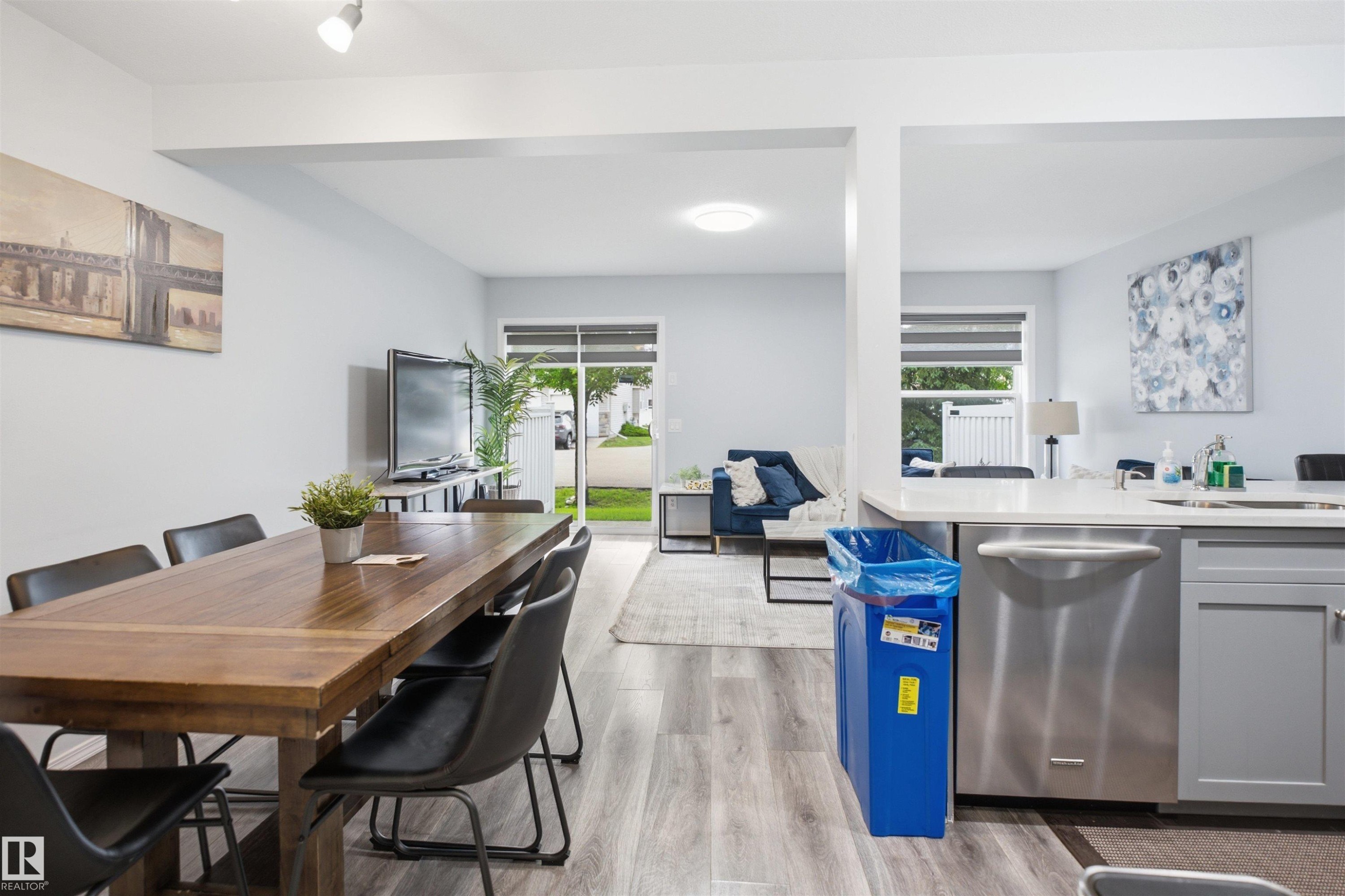 Spacious open-concept living area featuring wood-finish flooring, recessed lighting, and large windows with blinds - 92 230 Edwards Drive, Edmonton, AB