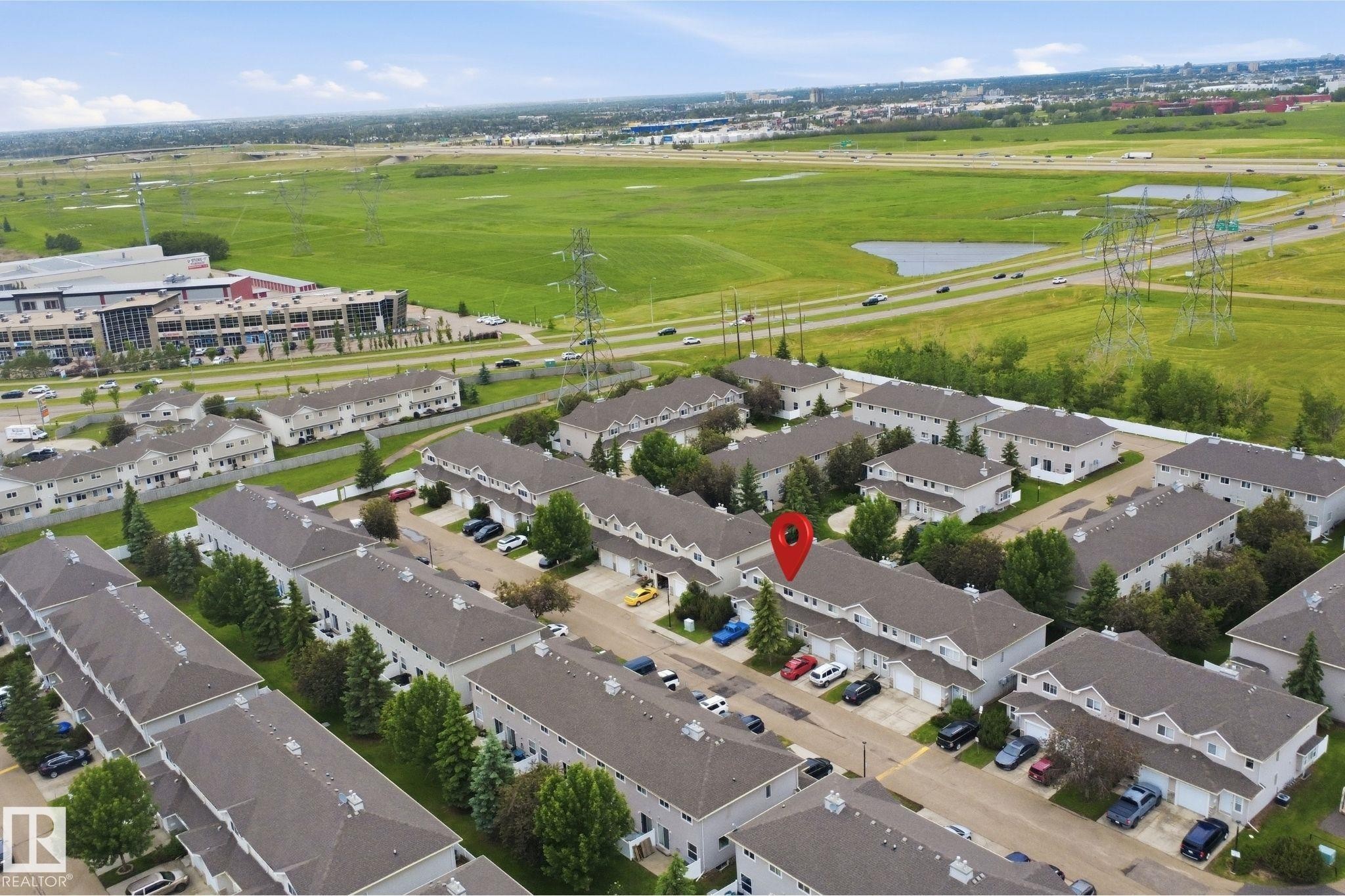 Aerial perspective of a multi-unit residential development with a backdrop of green fields and a highway - 92 230 Edwards Drive, Edmonton, AB
