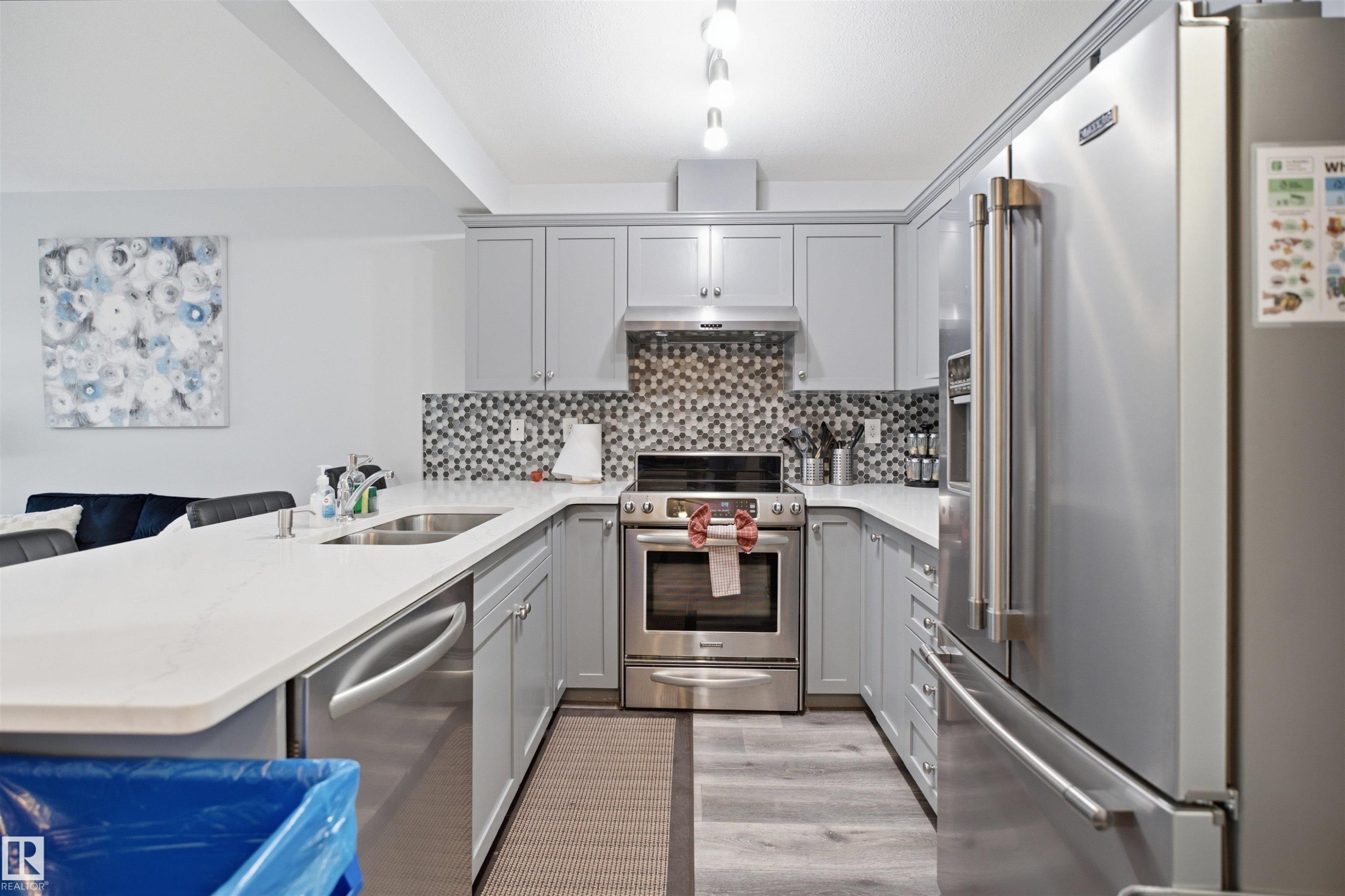 Modern kitchen featuring light gray cabinetry, stainless steel appliances, a mosaic tile backsplash, and light-tone countertops - 92 230 Edwards Drive, Edmonton, AB