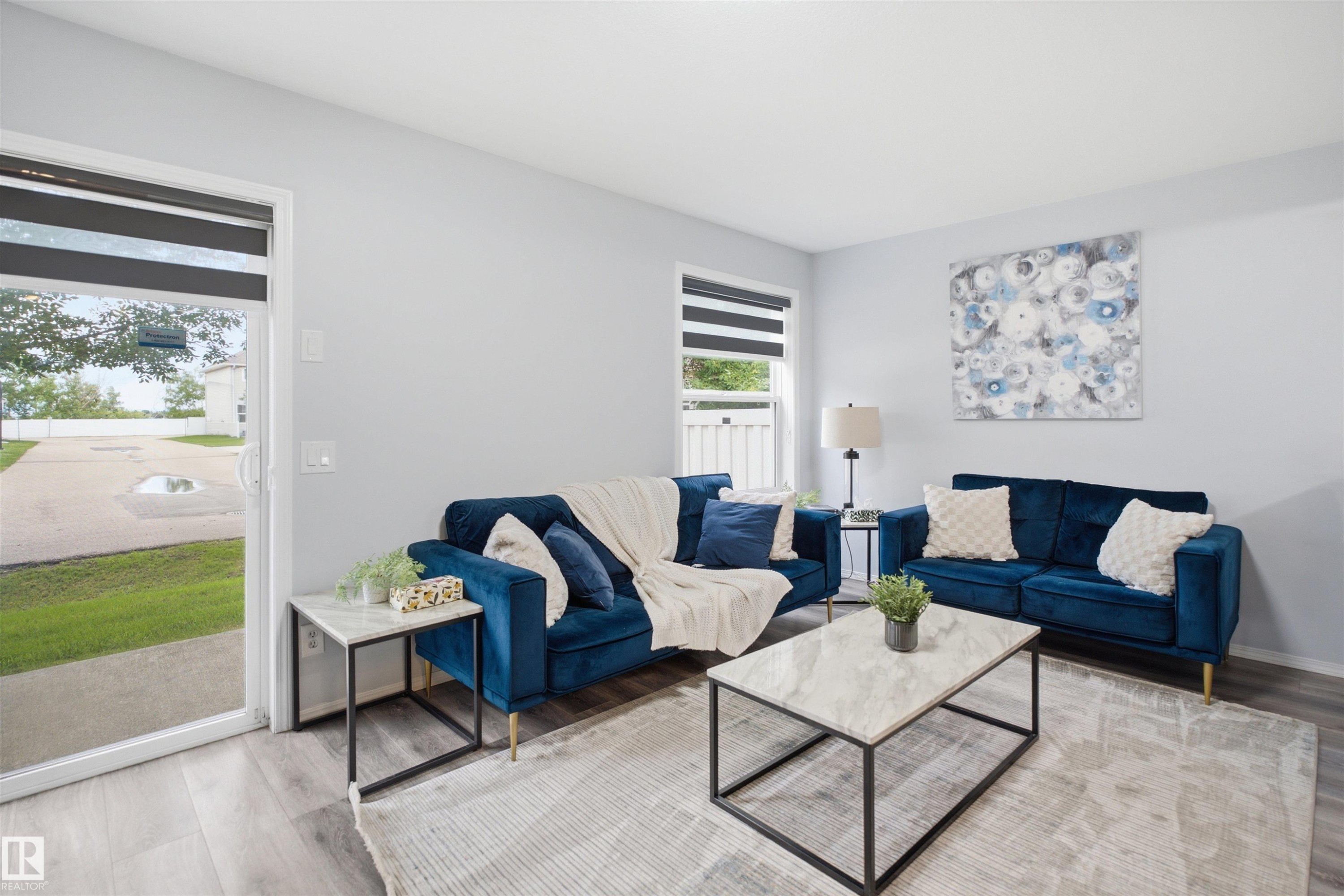 Living area featuring light gray walls, wood-finish flooring, a sliding glass door, and a window with horizontal blinds - 92 230 Edwards Drive, Edmonton, AB