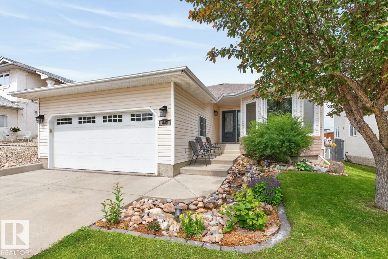 Cream-colored siding exterior featuring a multi-pane garage door, bay windows, and a black front door - 448 Ormsby Road Nw, Edmonton, AB - Outdoor