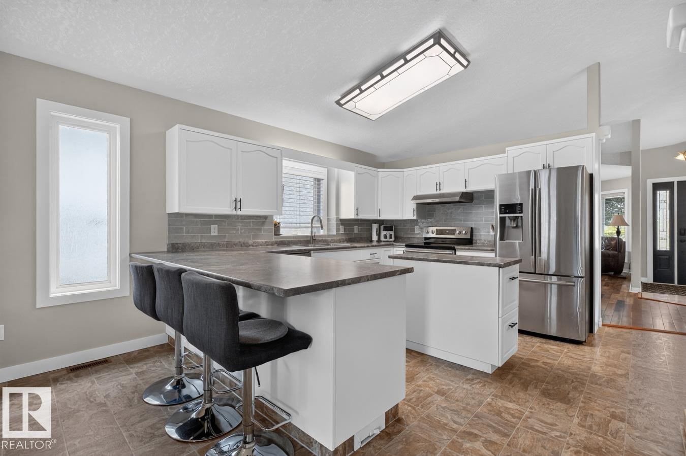 Spacious kitchen featuring white cabinetry, stainless steel appliances, a tiled backsplash, and a multi-purpose island with counter seating - 448 Ormsby Road Nw, Edmonton, AB - Indoor Photo Showing Kitchen