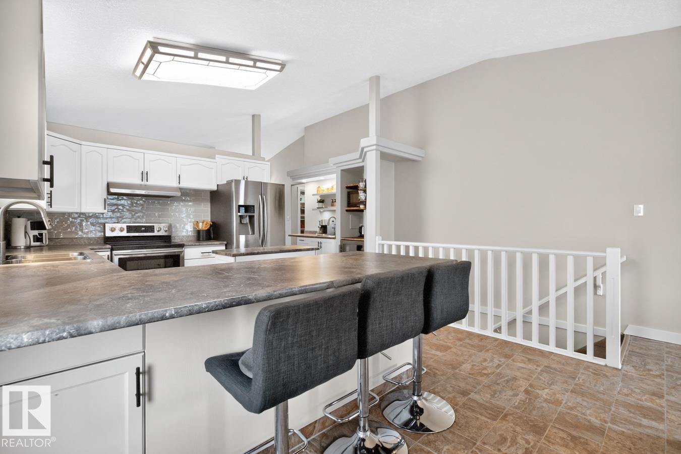 Kitchen featuring an eat-at island with a textured countertop, white cabinetry with dark hardware, stainless steel appliances, a tile backsplash, and tile flooring - 448 Ormsby Road Nw, Edmonton, AB - Indoor Photo Showing Kitchen