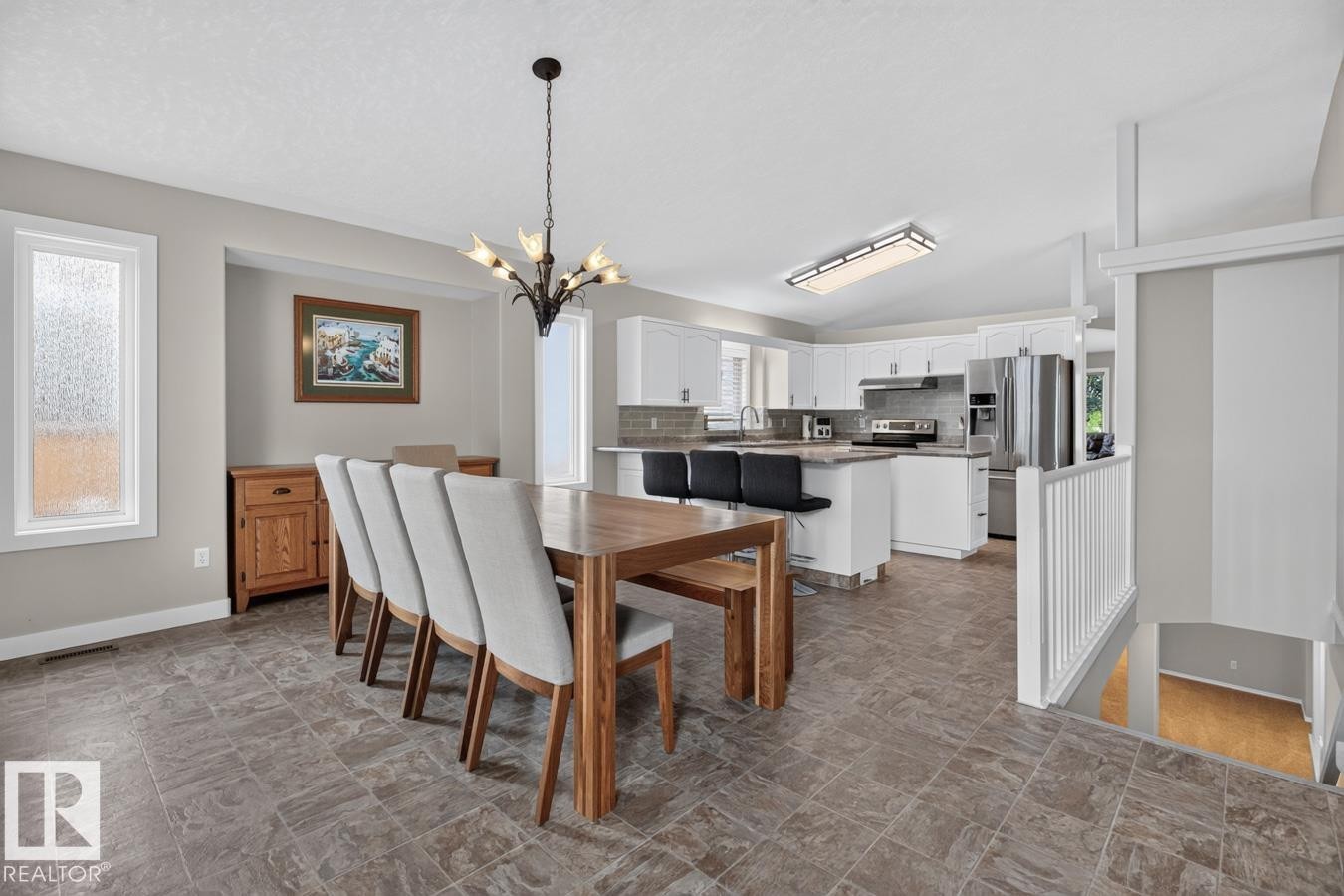 Open-concept dining and kitchen area featuring tile flooring, white cabinetry, stainless steel appliances, a kitchen island with seating, and a decorative chandelier - 448 Ormsby Road Nw, Edmonton, AB - Indoor Photo Showing Dining Room