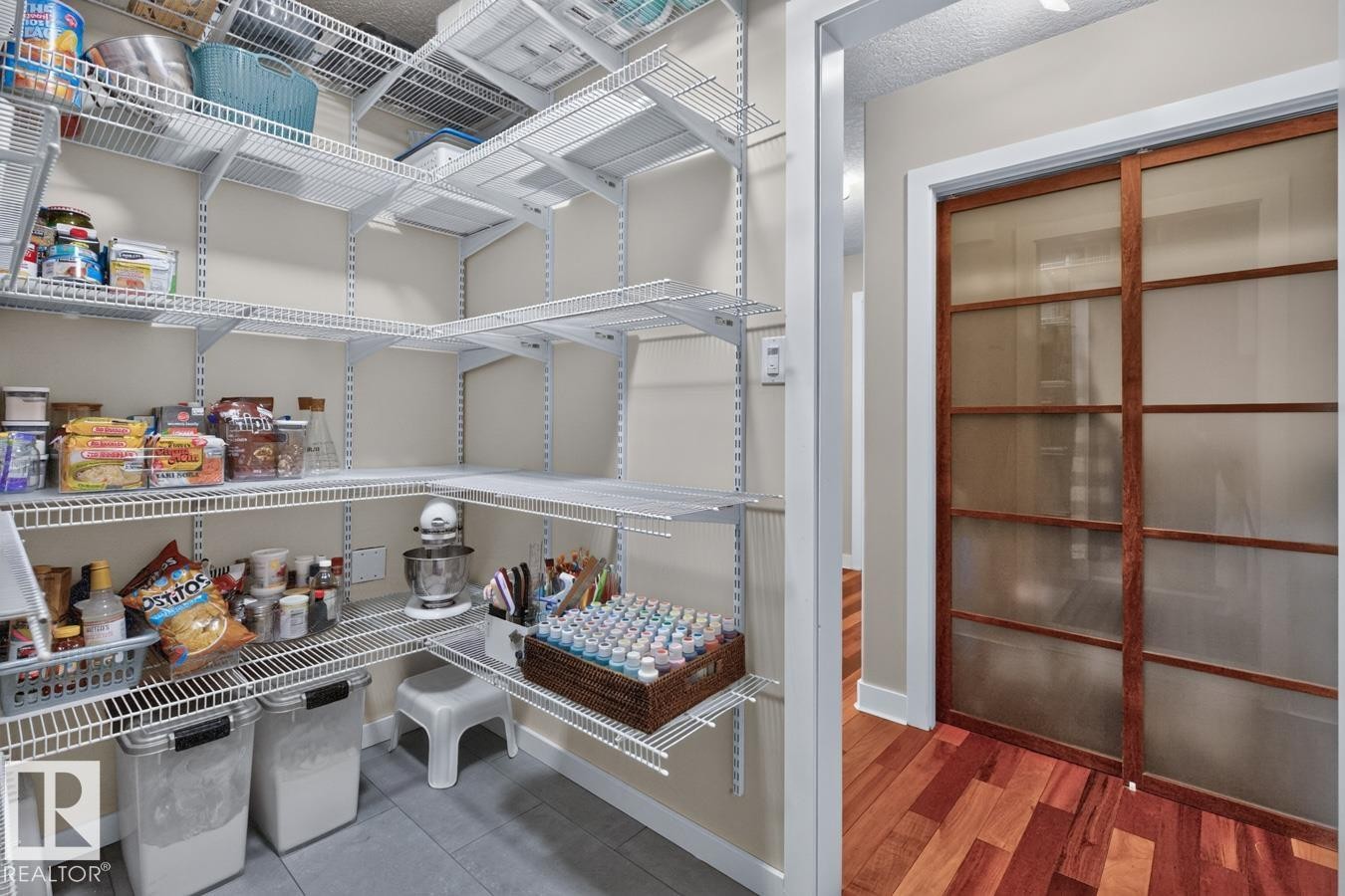 Spacious pantry featuring extensive wire shelving, durable tile flooring, and a nearby room with wood-finish flooring and a frosted glass sliding door - 448 Ormsby Road Nw, Edmonton, AB - Indoor With Storage