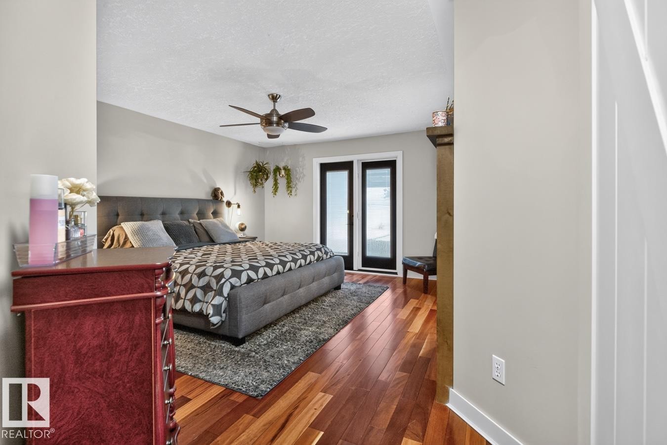 Bedroom featuring wood-finish flooring, a ceiling fan, and double French doors with black frames - 448 Ormsby Road Nw, Edmonton, AB - Indoor Photo Showing Bedroom