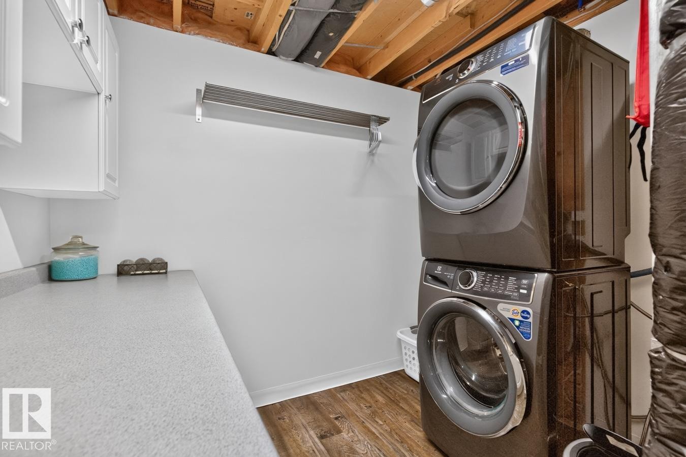 Laundry area featuring wood-finish flooring, white cabinetry, and a stacked washer and dryer unit - 448 Ormsby Road Nw, Edmonton, AB - Indoor Photo Showing Laundry Room