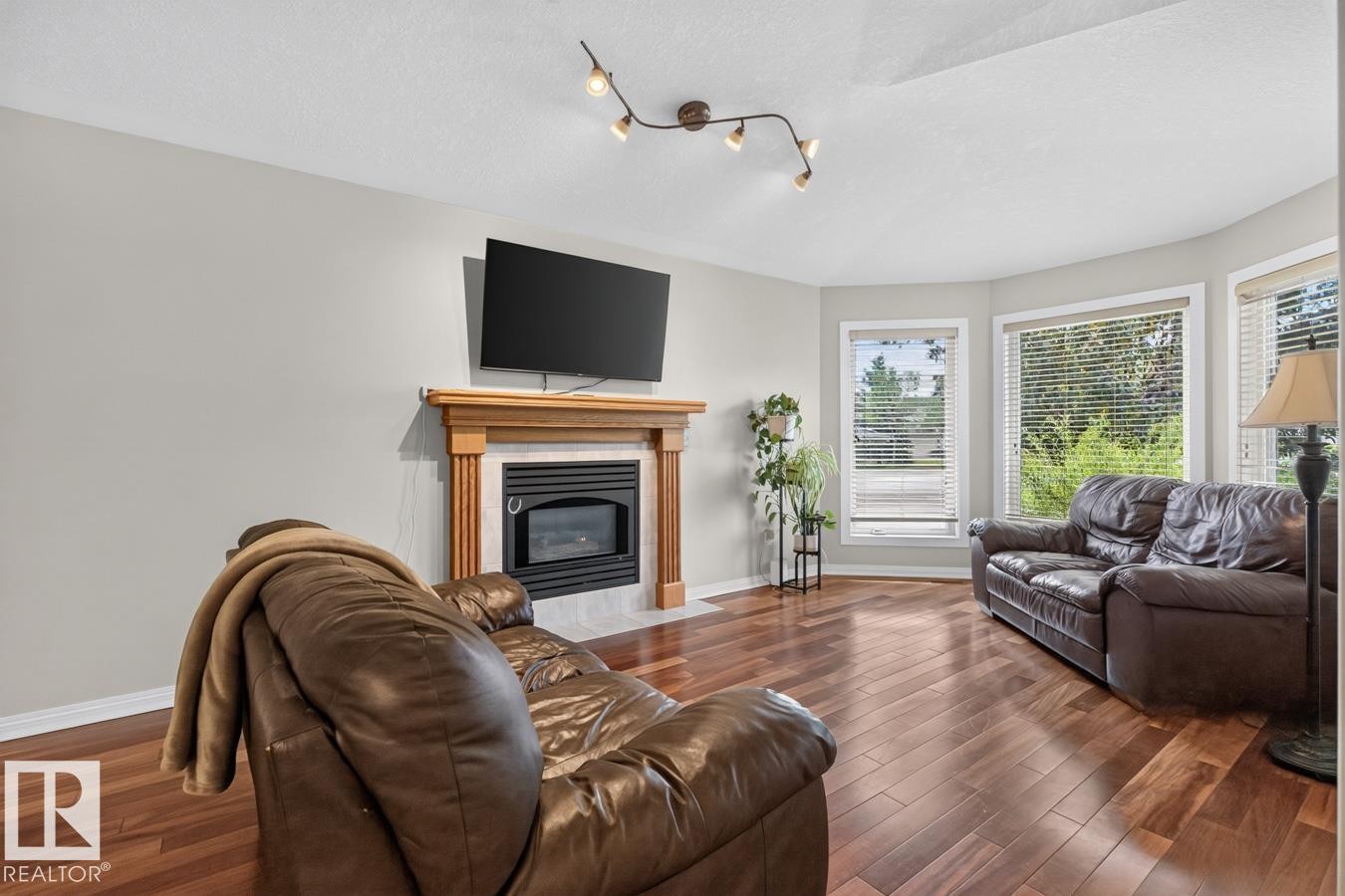 Living area featuring wood-finish flooring, a fireplace with a light-toned wood mantel and tiled surround, and multiple bay windows - 448 Ormsby Road Nw, Edmonton, AB - Indoor Photo Showing Living Room With Fireplace