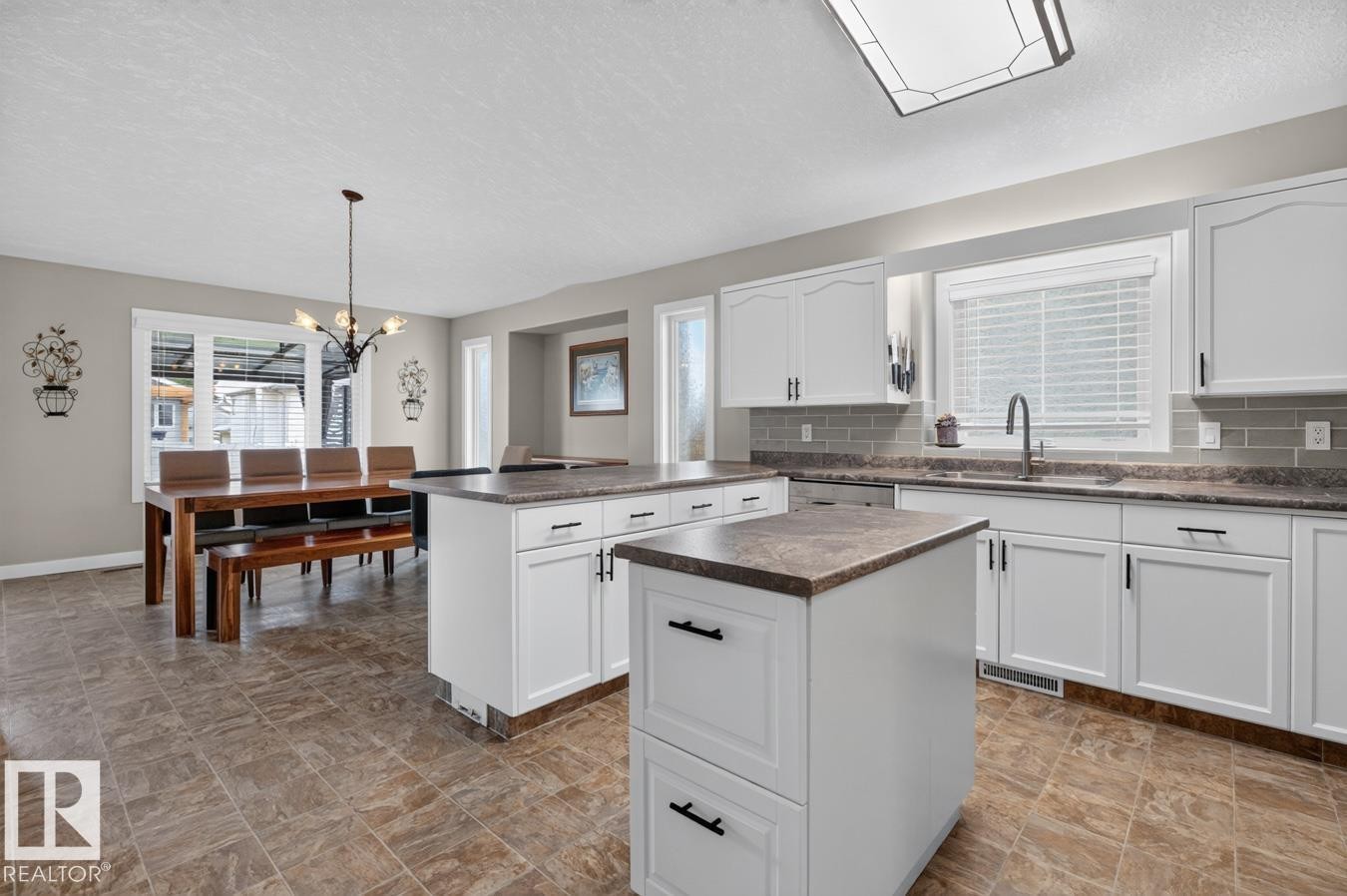 Open-concept kitchen and dining area featuring white cabinetry, dual islands with stone-finish countertops, subway tile backsplash, and tile flooring - 448 Ormsby Road Nw, Edmonton, AB - Indoor Photo Showing Kitchen