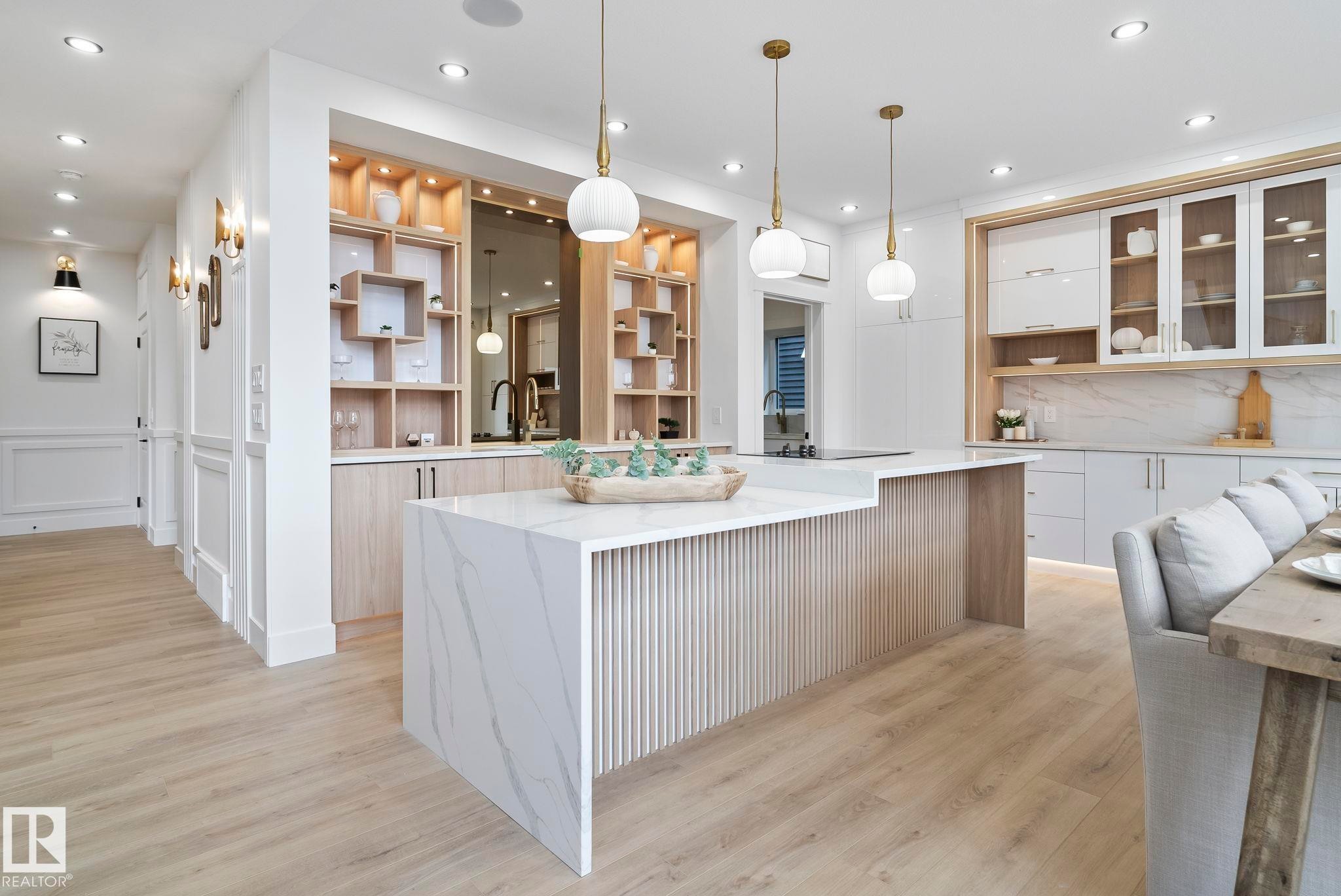 Open-concept kitchen featuring a waterfall island with a fluted wood base, light wood-finish flooring, recessed lighting, and stylish pendant light fixtures - 13152 187 Avenue, Edmonton, AB