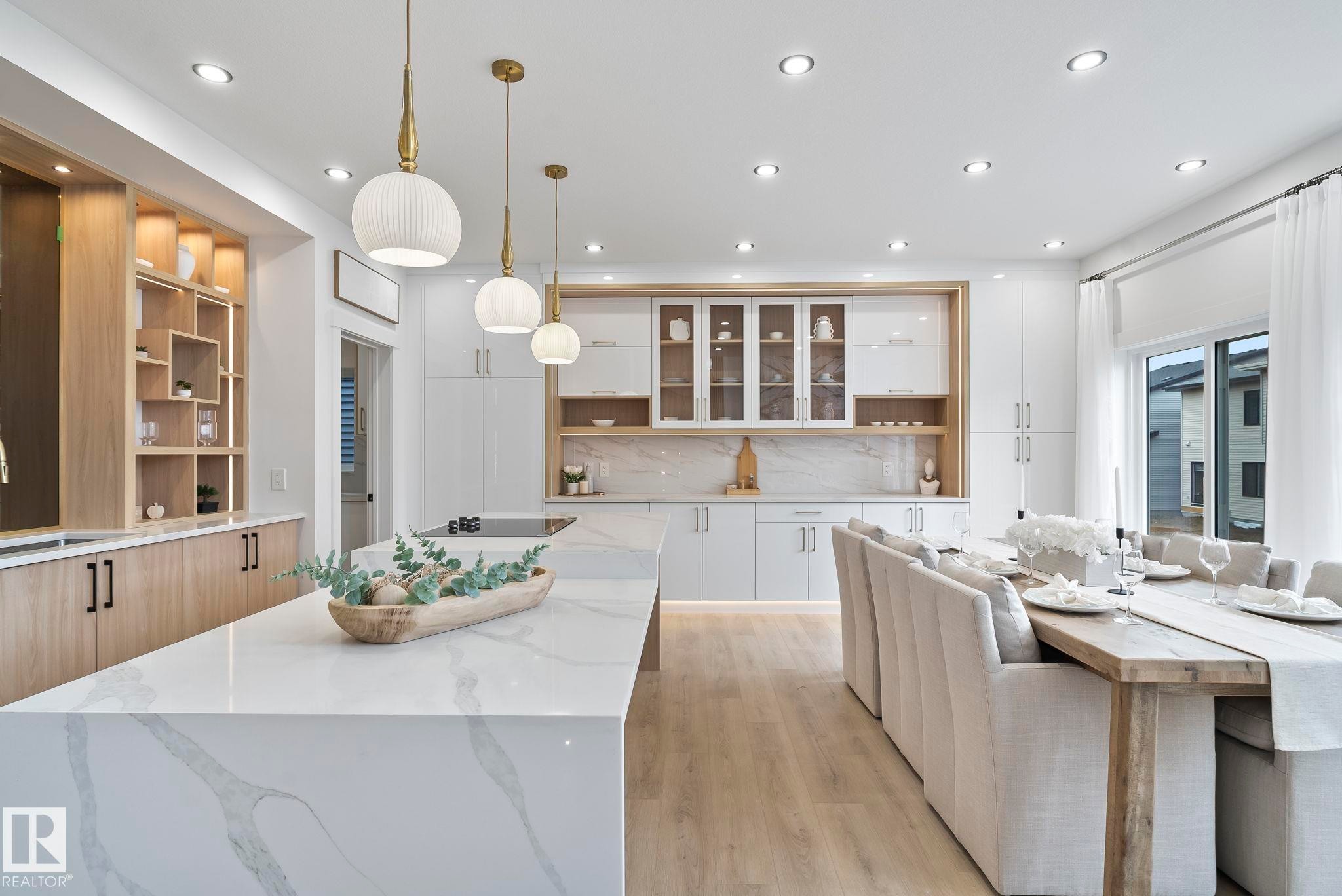 Open-concept kitchen and dining area featuring a waterfall-edge island with an integrated cooktop, pendant lighting, built-in shelving with accent lighting, and wood-finish flooring - 13152 187 Avenue, Edmonton, AB