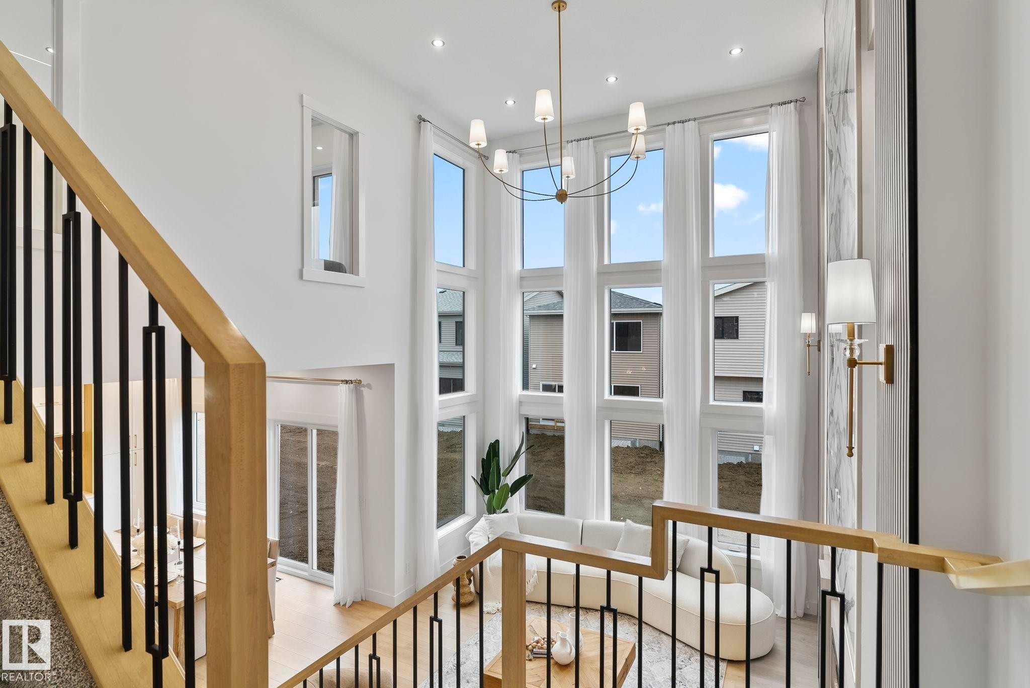 Two-story living area with expansive floor-to-ceiling windows, a contemporary chandelier, and recessed lighting - 13152 187 Avenue, Edmonton, AB