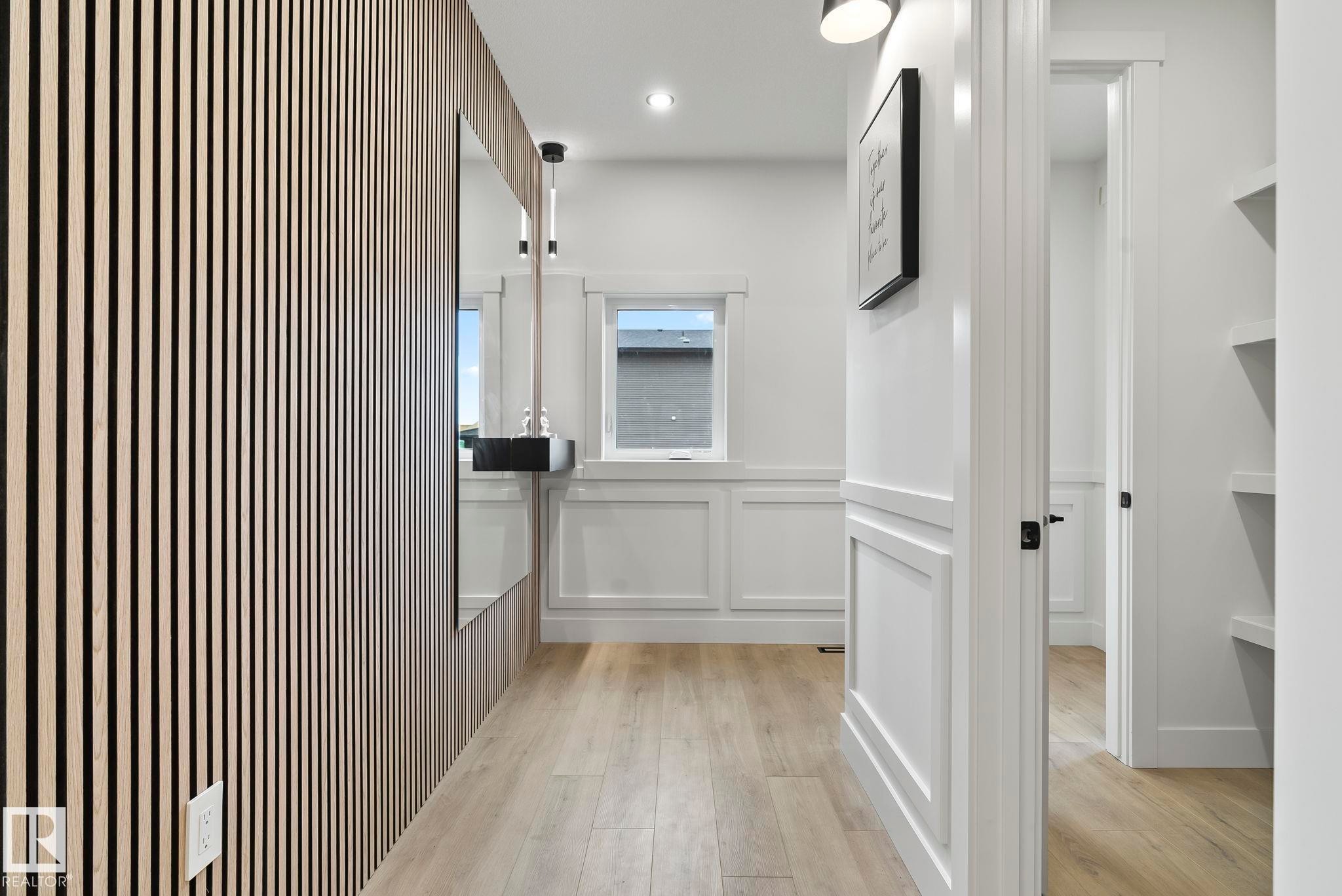 Hallway featuring a slatted wood-panel accent wall, wainscoting, wood-finish flooring, and recessed lighting - 13152 187 Avenue, Edmonton, AB