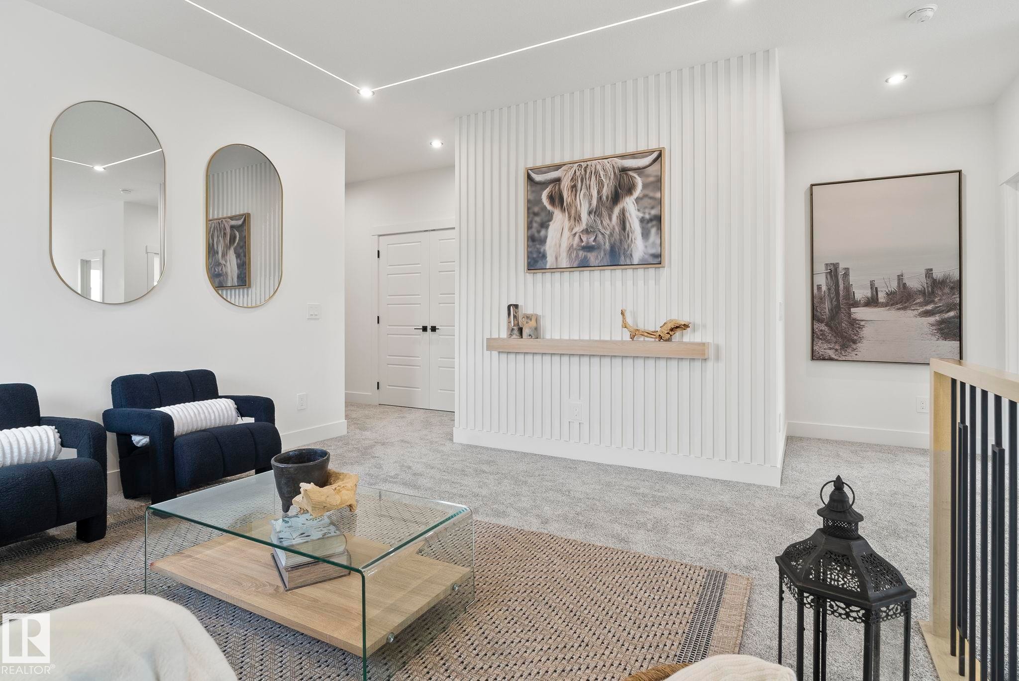 Spacious upper-level landing featuring light gray carpeting, a contemporary glass coffee table with a wood-finish base, and a white paneled accent wall with a floating wood-finish shelf - 13152 187 Avenue, Edmonton, AB
