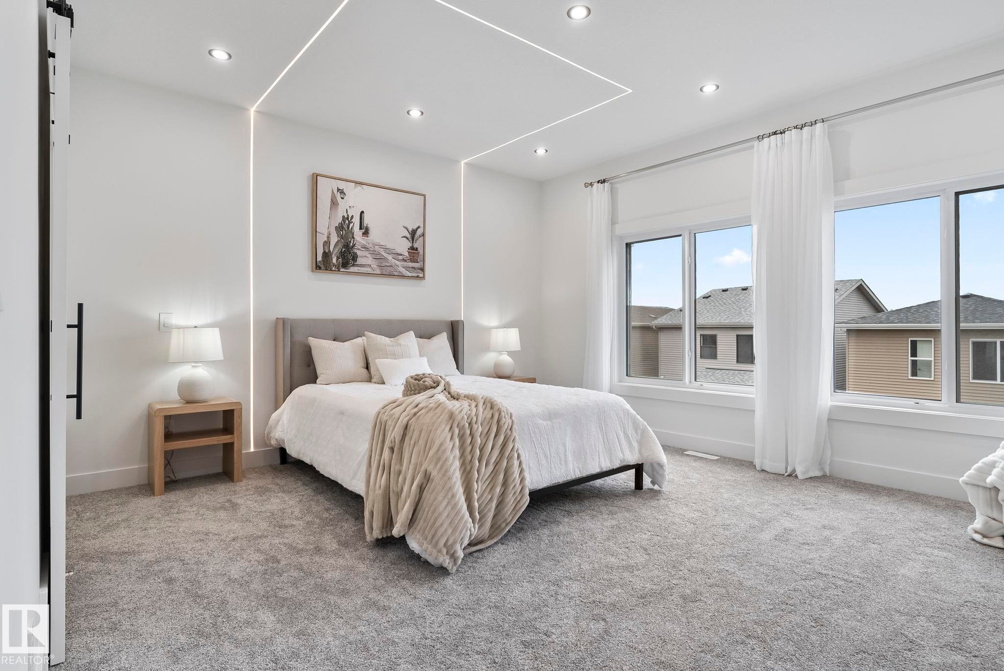 Bedroom featuring recessed ceiling lighting, integrated wall lighting, a large window array with white trim, and a barn door with a matte black handle - 13152 187 Avenue, Edmonton, AB