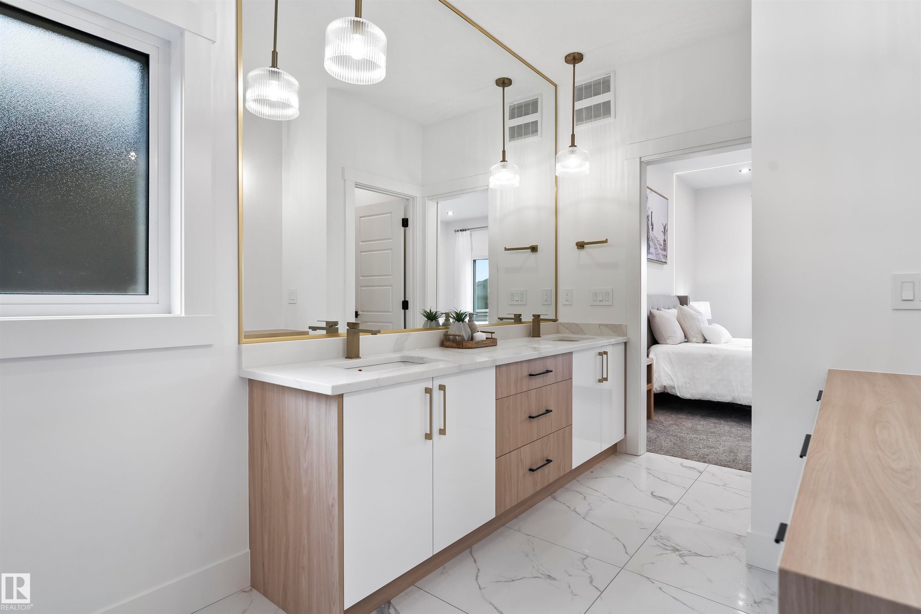 Dual vanity featuring a light wood-finish and white cabinetry, a light-toned countertop, and dual gold-finish fixtures - 13152 187 Avenue, Edmonton, AB