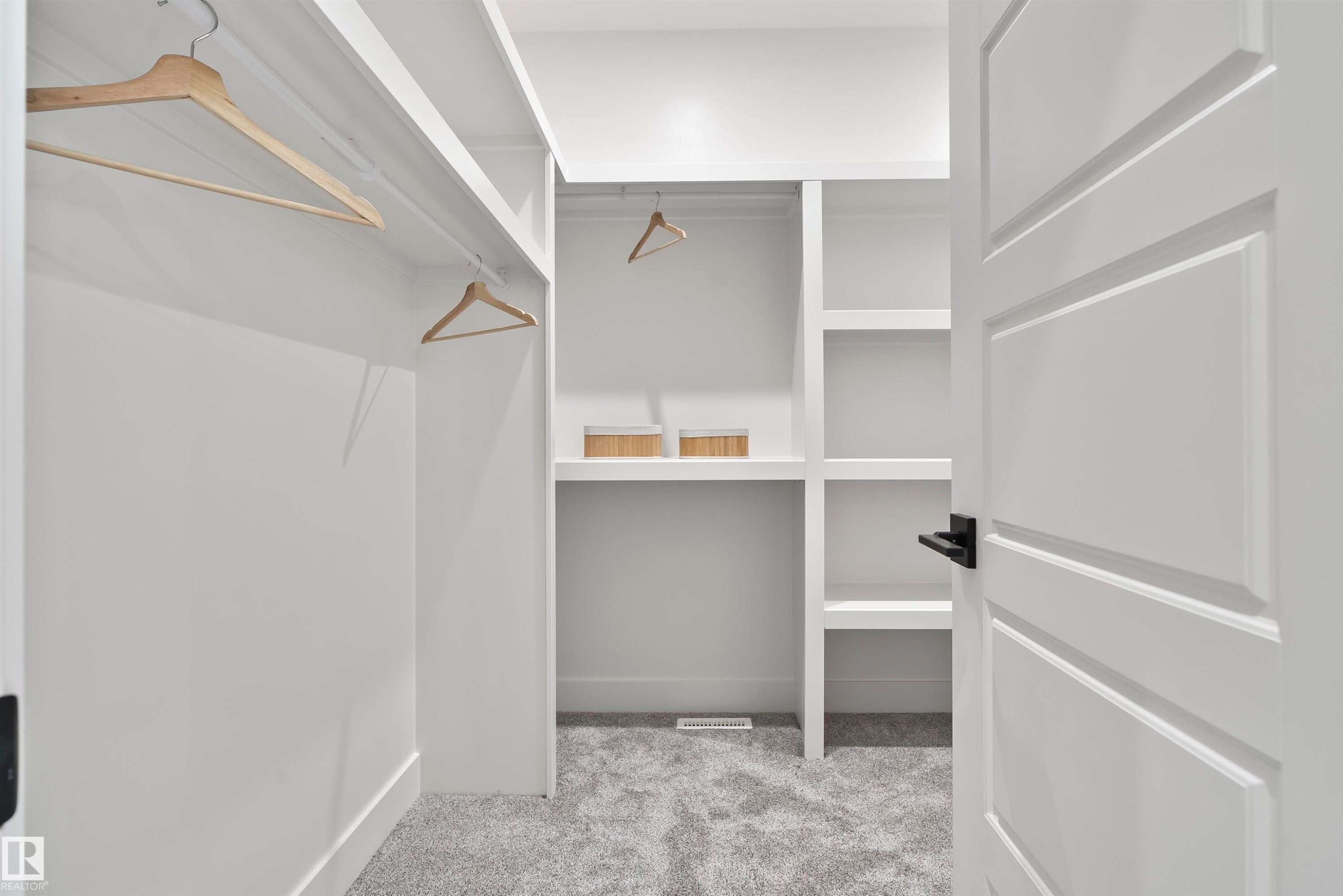 Spacious walk-in closet featuring built-in shelving, hanging rods, light gray carpet, and a white paneled door with matte black hardware - 13152 187 Avenue, Edmonton, AB