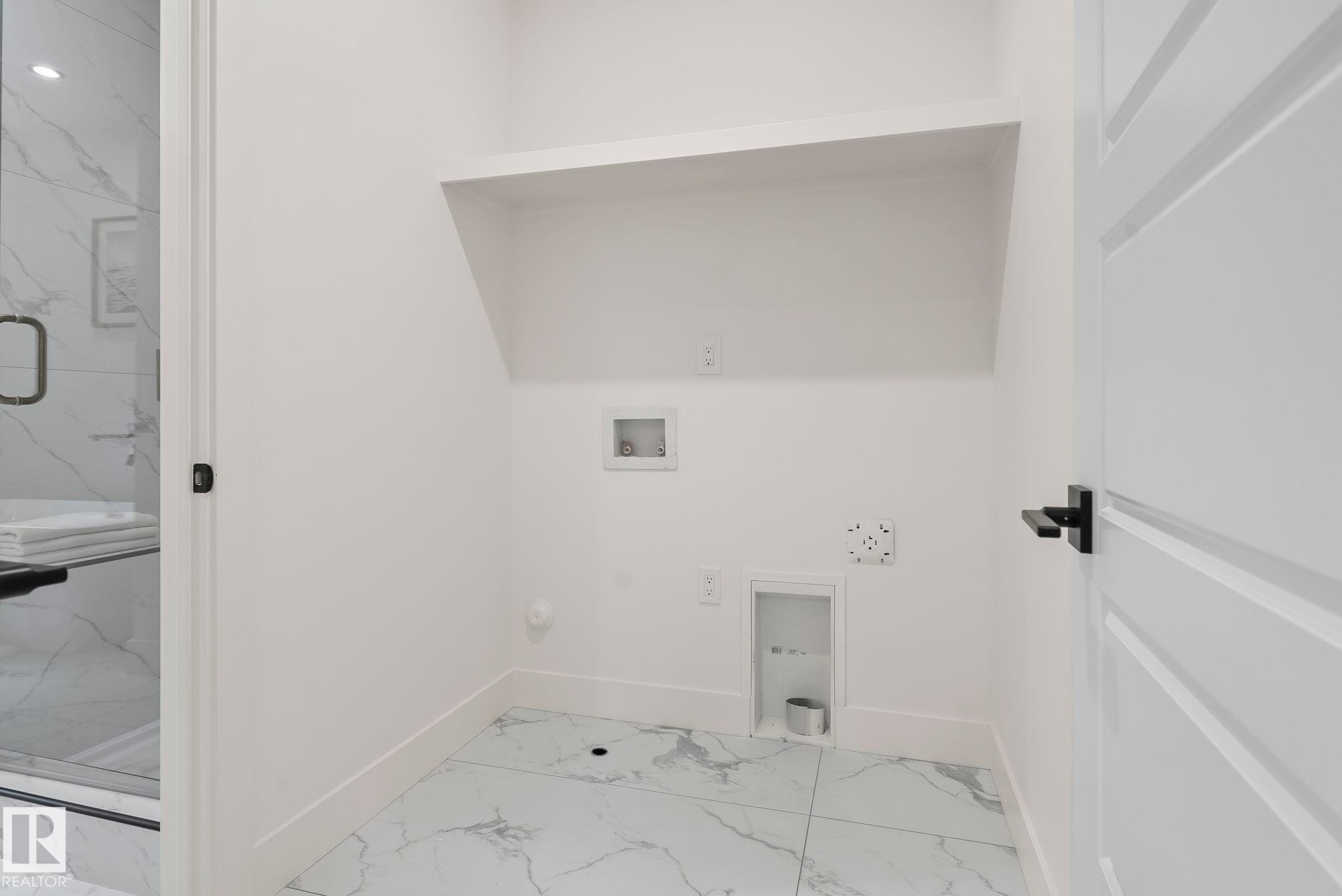 Dedicated laundry space featuring a built-in shelving unit and white tile flooring with grey veining - 13152 187 Avenue, Edmonton, AB