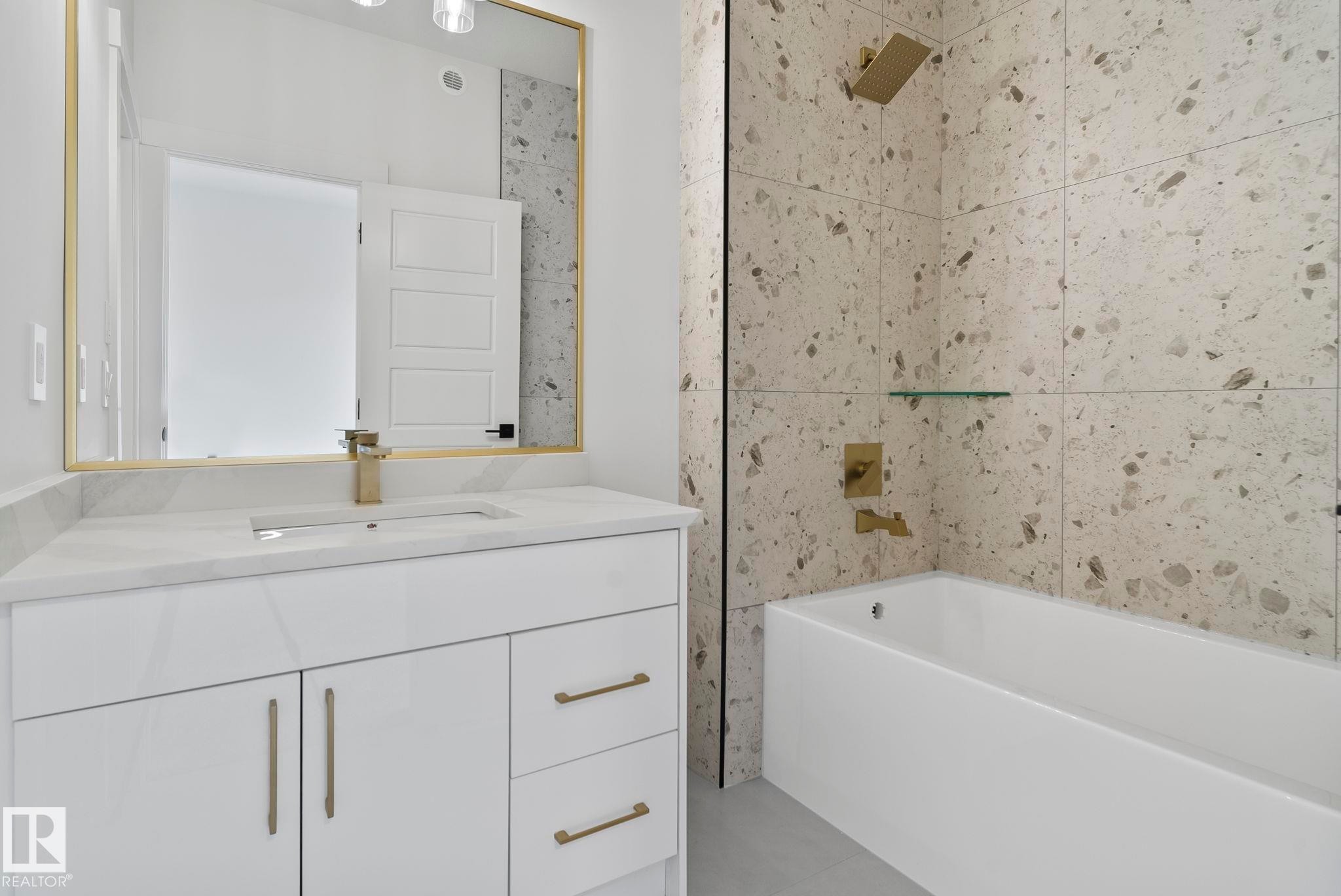 Contemporary bathroom featuring a white vanity with integrated sink, gold-finish fixtures, and a large mirror - 13152 187 Avenue, Edmonton, AB