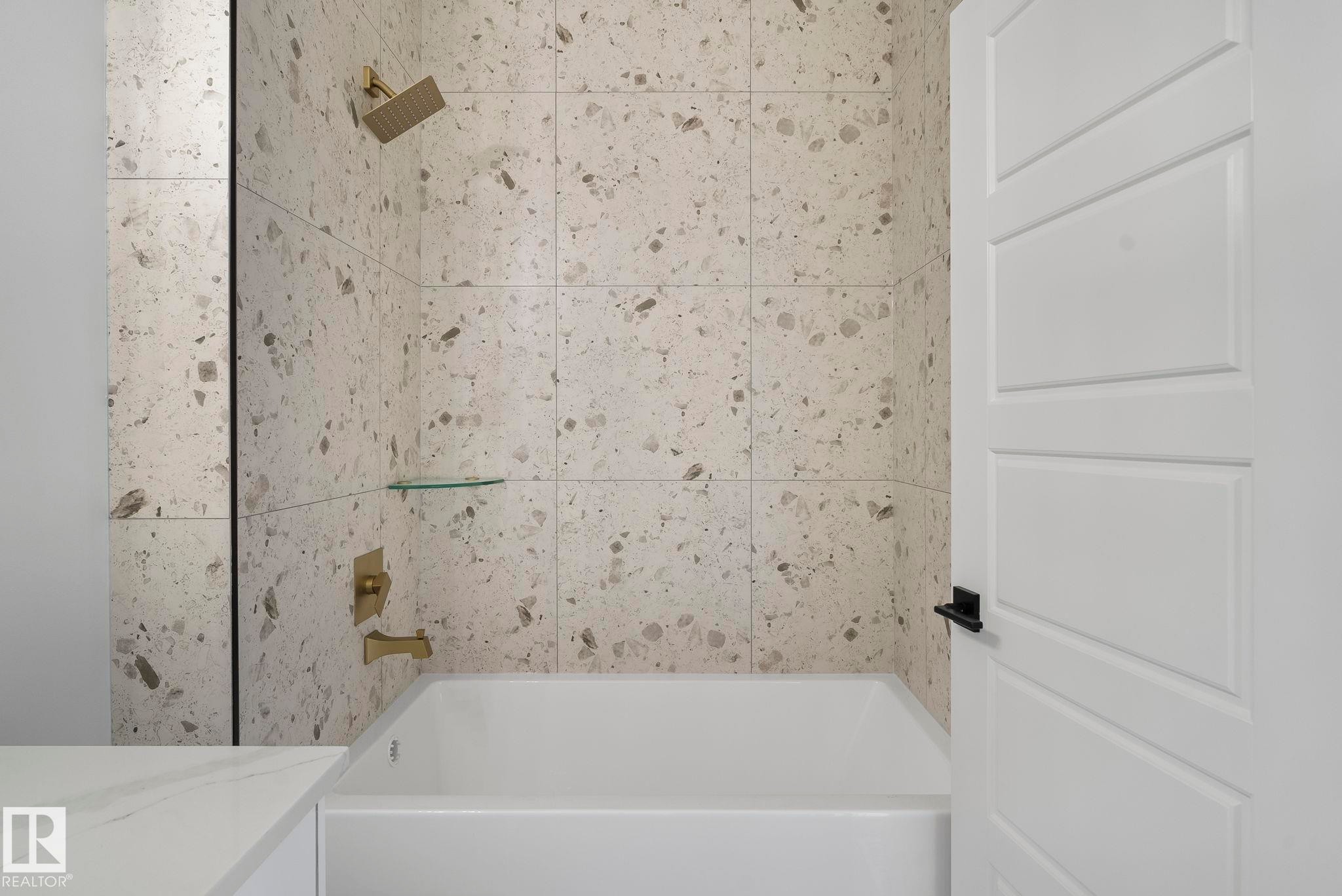 Modern bathroom featuring a built-in tub, tiled shower surround with gold-finish fixtures, and a glass shower shelf - 13152 187 Avenue, Edmonton, AB