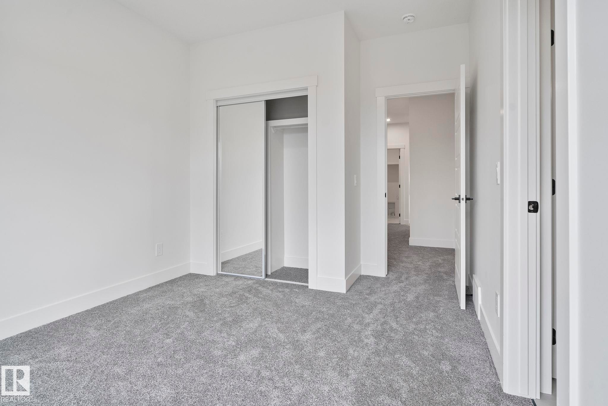 Carpeted interior room featuring a mirrored closet, white baseboards, and a neutral wall color - 13152 187 Avenue, Edmonton, AB