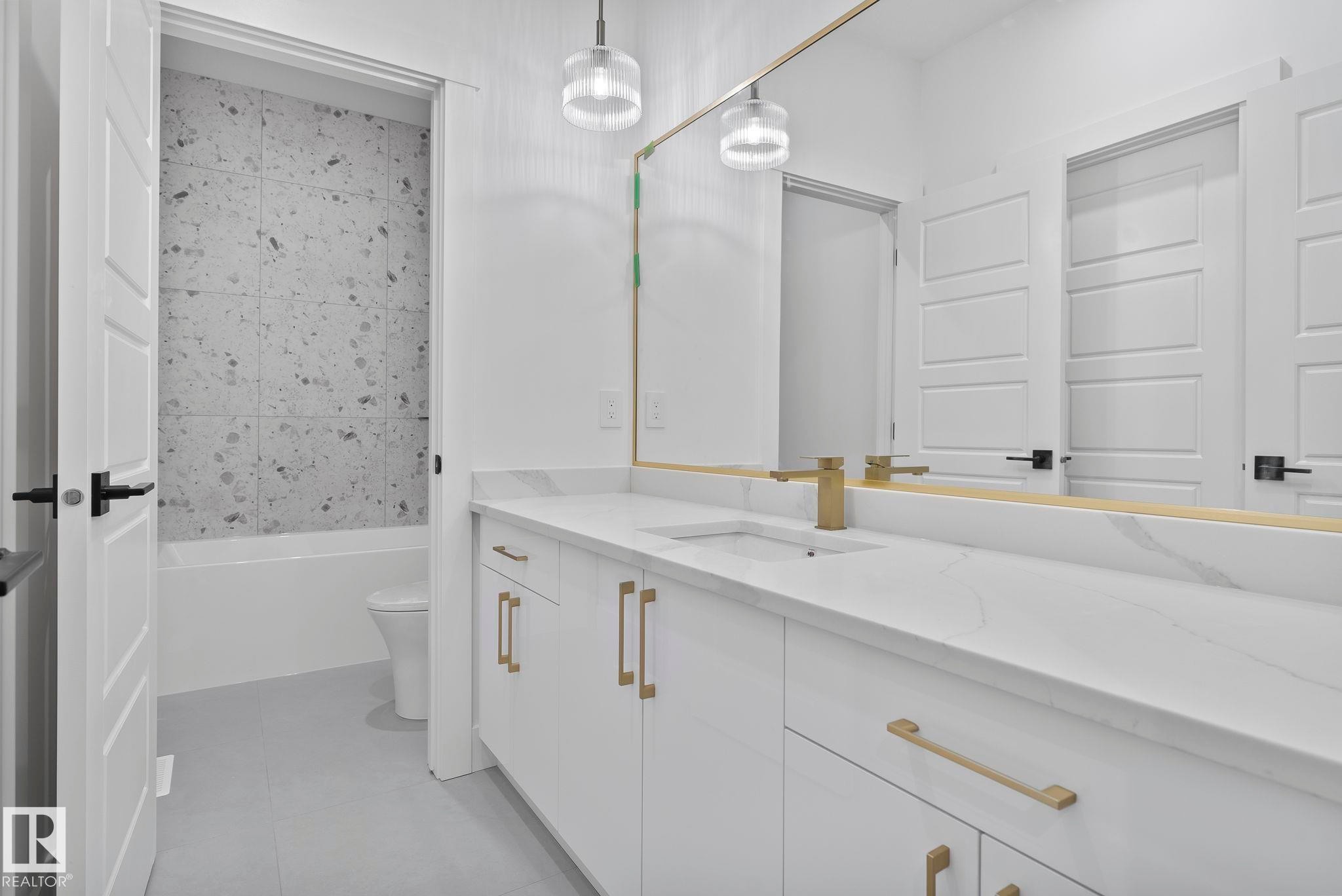 Double vanity featuring white cabinetry with gold-finish hardware, a single undermount sink, and a white countertop with subtle veining - 13152 187 Avenue, Edmonton, AB