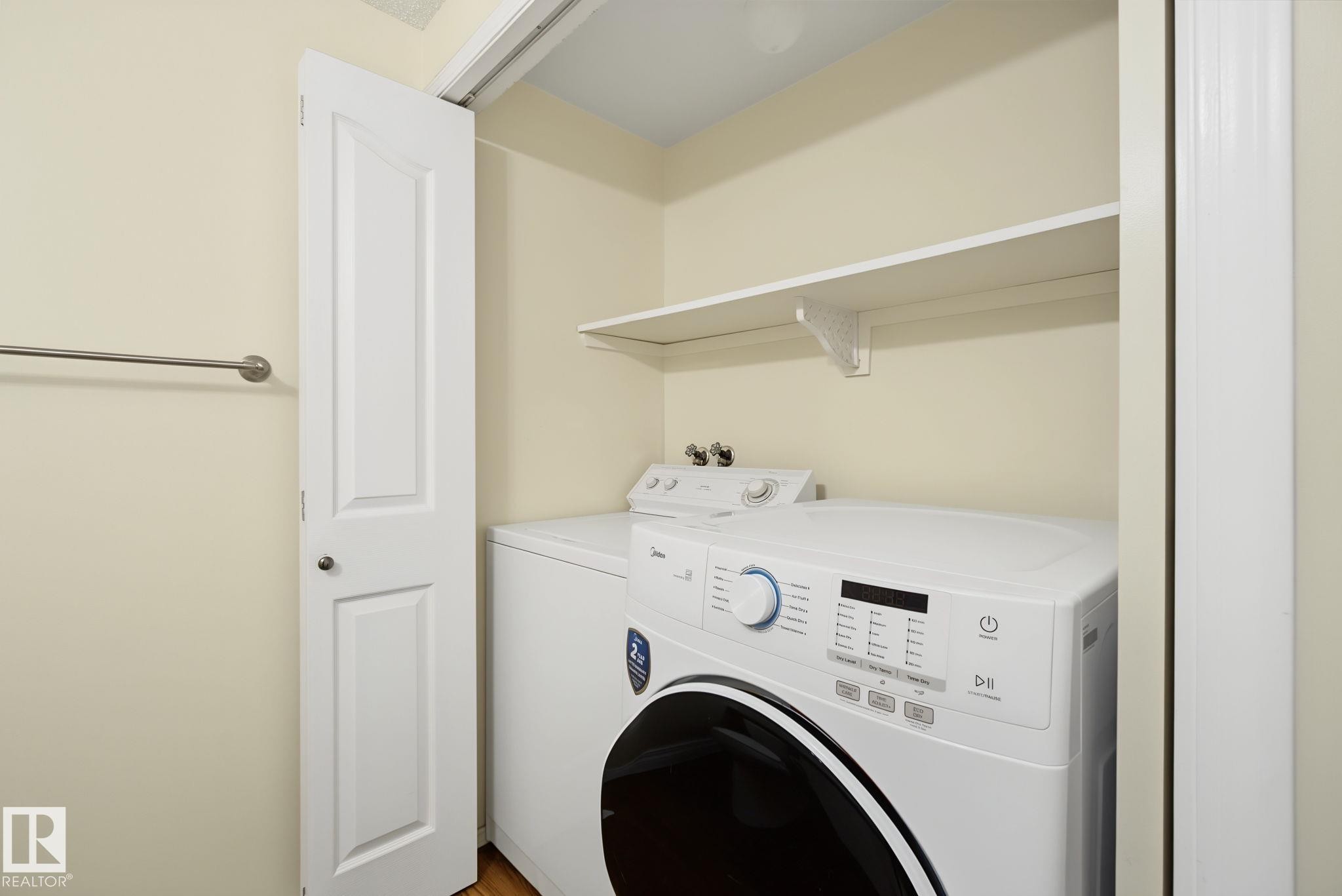 Dedicated laundry closet featuring a built-in shelf, white paneled bifold door, and wood-finish flooring - 4259 29 Avenue, Edmonton, AB