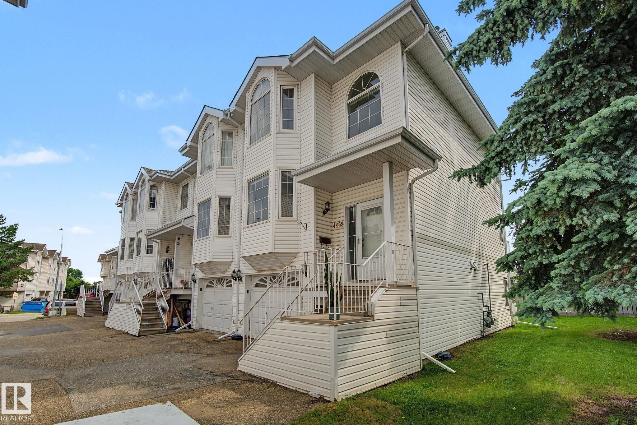 Multi-level townhouse exterior featuring white siding, multiple bay windows with arched transoms, and an integrated single-car garage - 4259 29 Avenue, Edmonton, AB