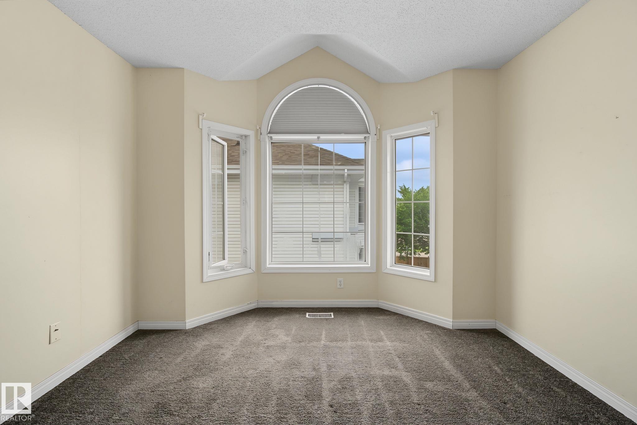 Bay window with an arched transom window, neutral-toned walls, textured ceiling, and gray patterned carpet - 4259 29 Avenue, Edmonton, AB