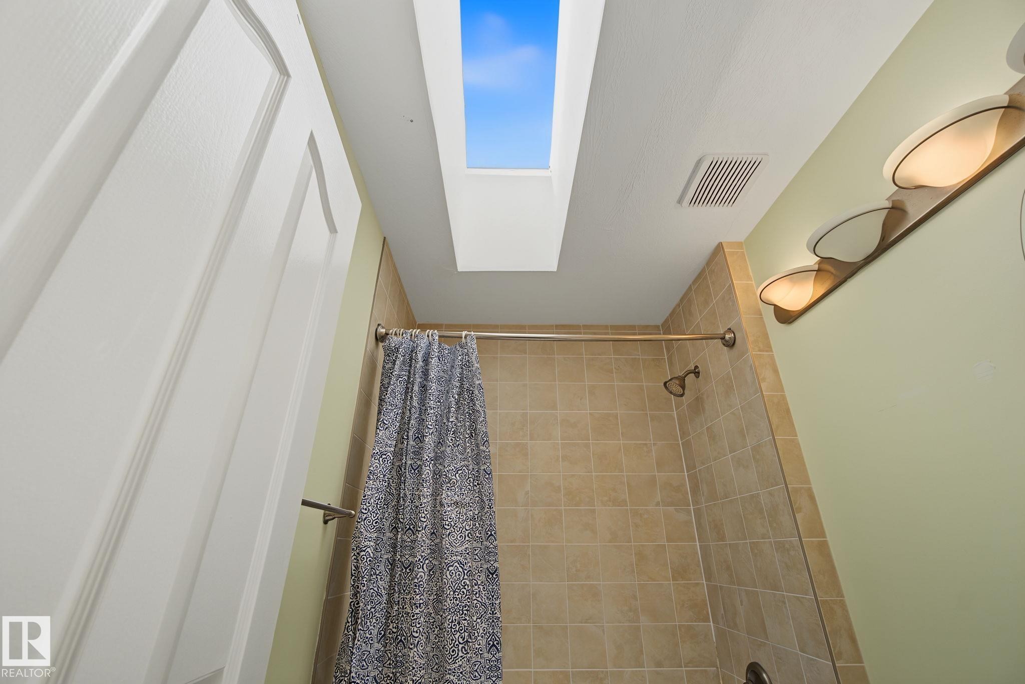 Bathroom featuring a skylight, full wall tile, built-in shower, and vanity lighting fixture - 4259 29 Avenue, Edmonton, AB