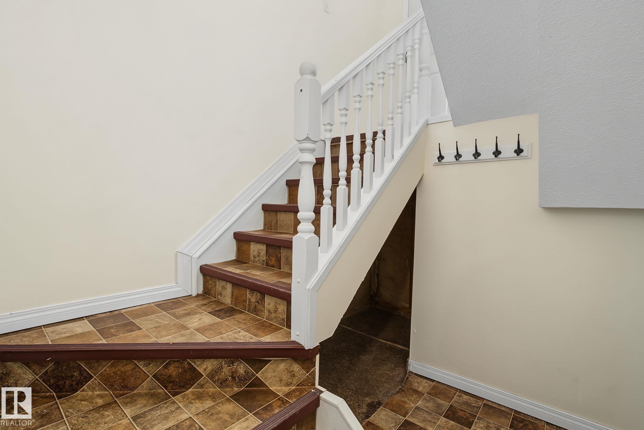 Staircase featuring a white balustrade and patterned brown floor tiles - 4259 29 Avenue, Edmonton, AB