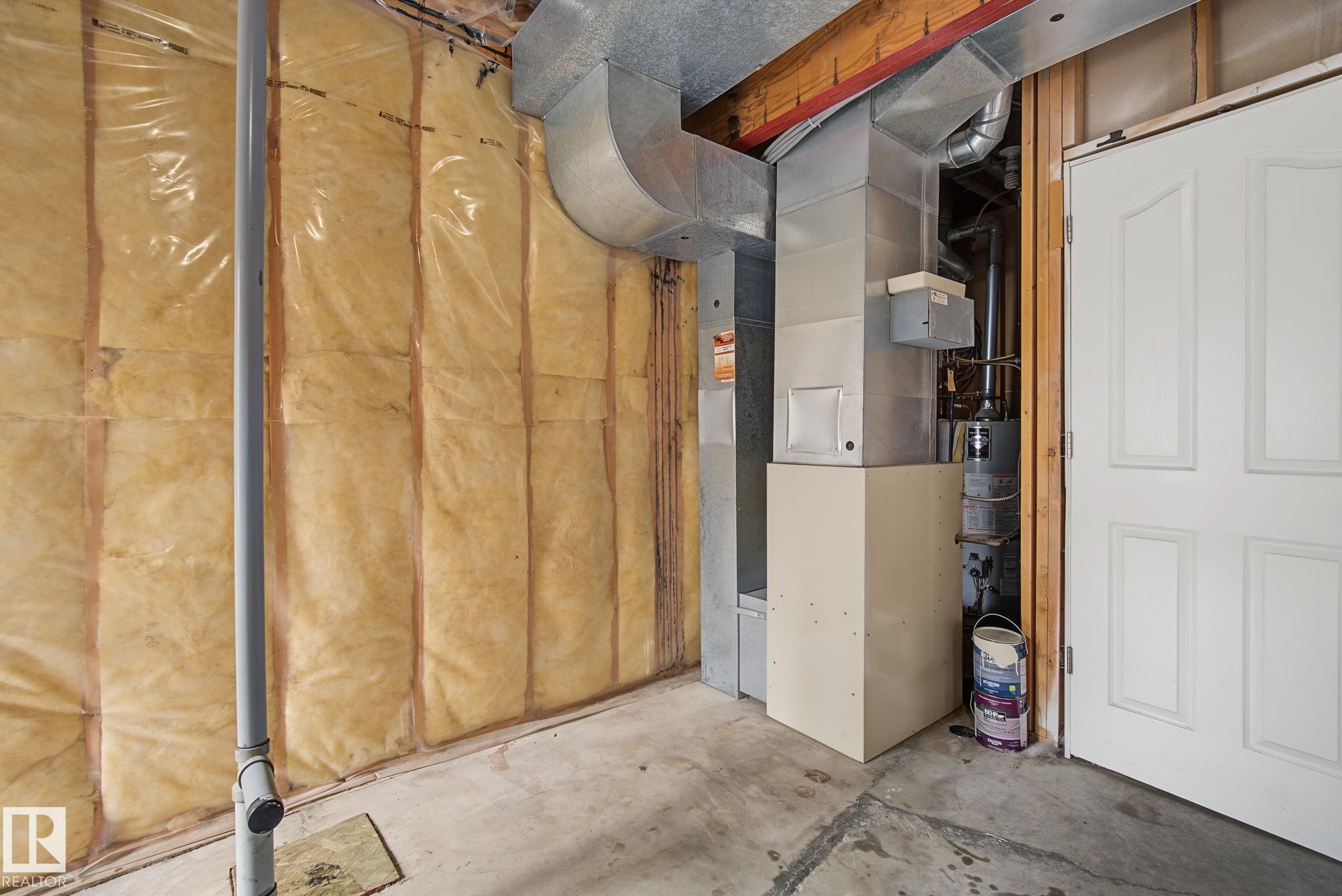 Partial basement featuring exposed concrete flooring, insulated walls, visible ductwork, and a white panel door - 4259 29 Avenue, Edmonton, AB
