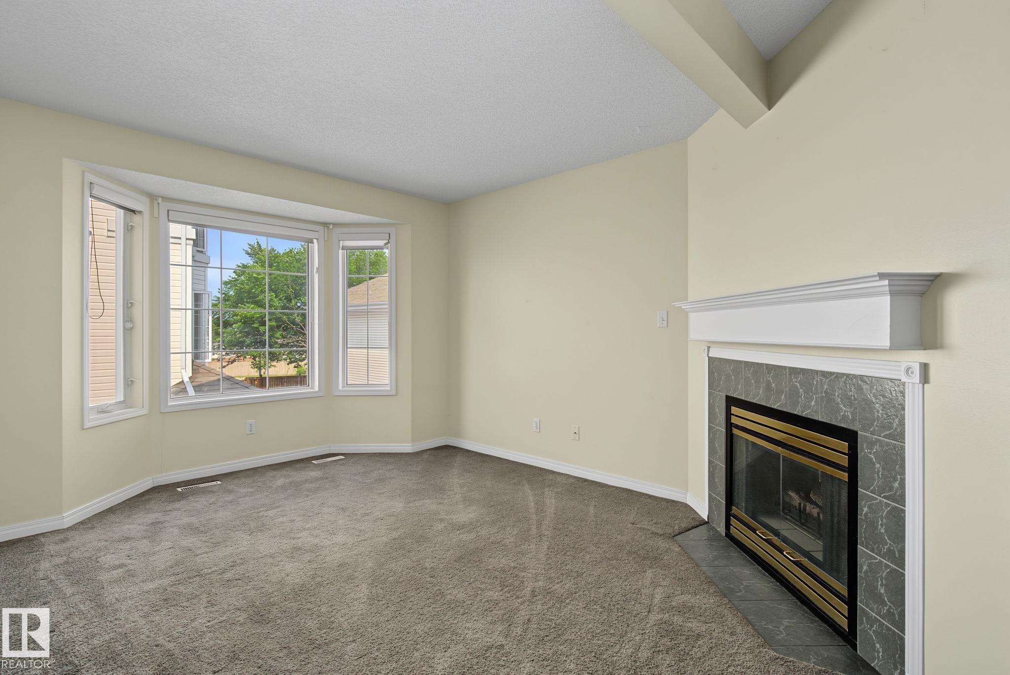 Light-filled interior featuring a bay window, wall-to-wall carpeting, a fireplace with a slate-look tile surround and white mantel, and neutral wall paint - 4259 29 Avenue, Edmonton, AB