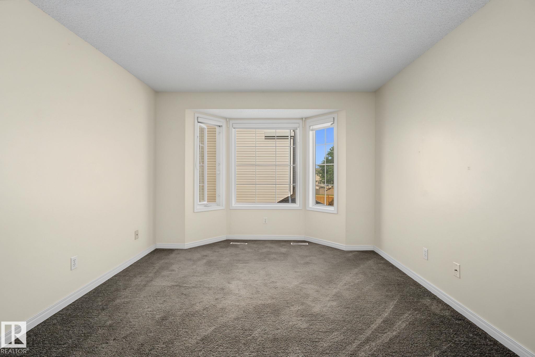 Recessed bay window with multiple panes, neutral wall paint, textured ceiling, and dark grey carpet flooring - 4259 29 Avenue, Edmonton, AB