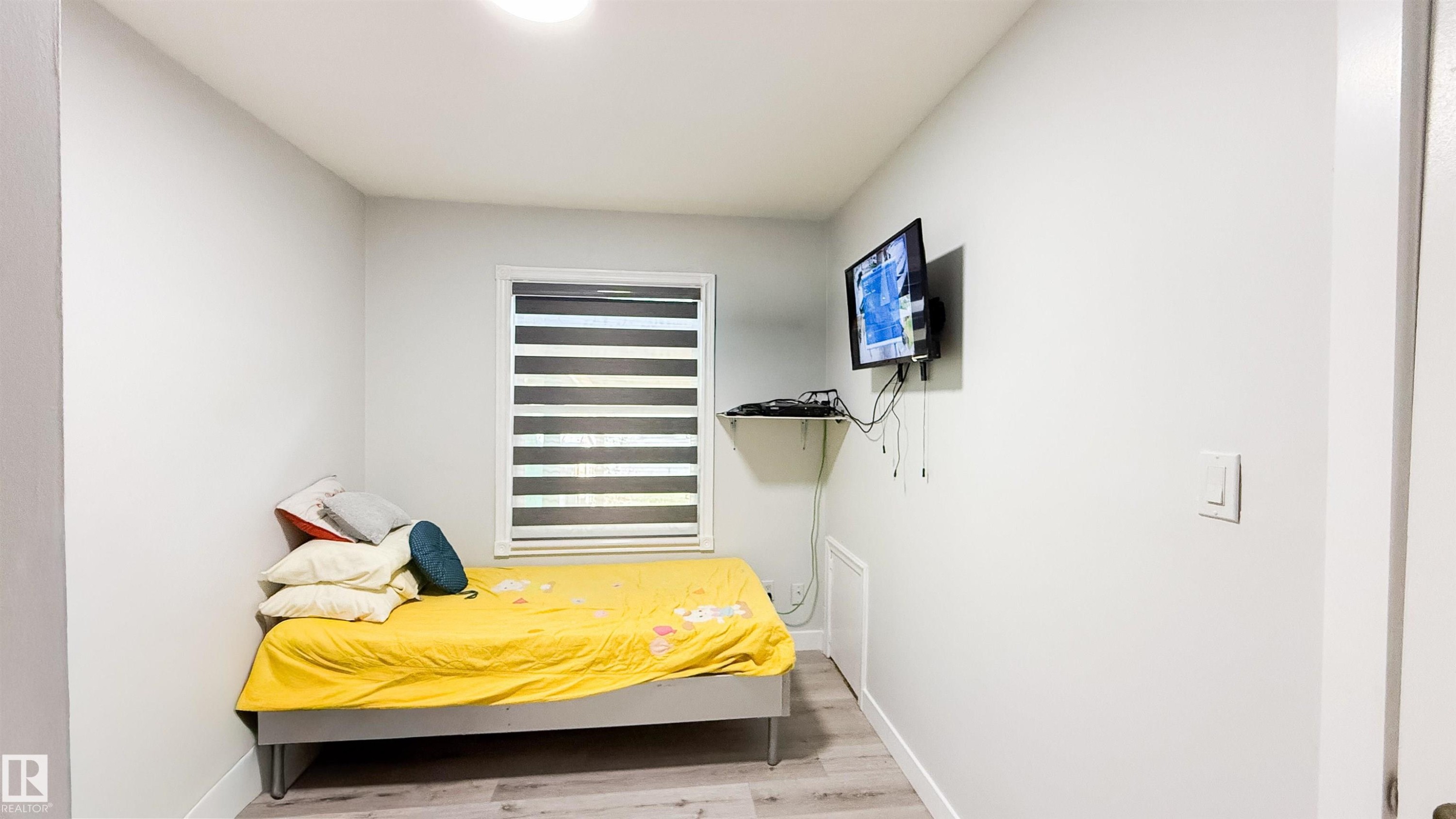 Room featuring light gray wall paint, wood-finish flooring, and a window with horizontal blinds - 12005 40 St Nw, Edmonton, AB - Indoor Photo Showing Bedroom