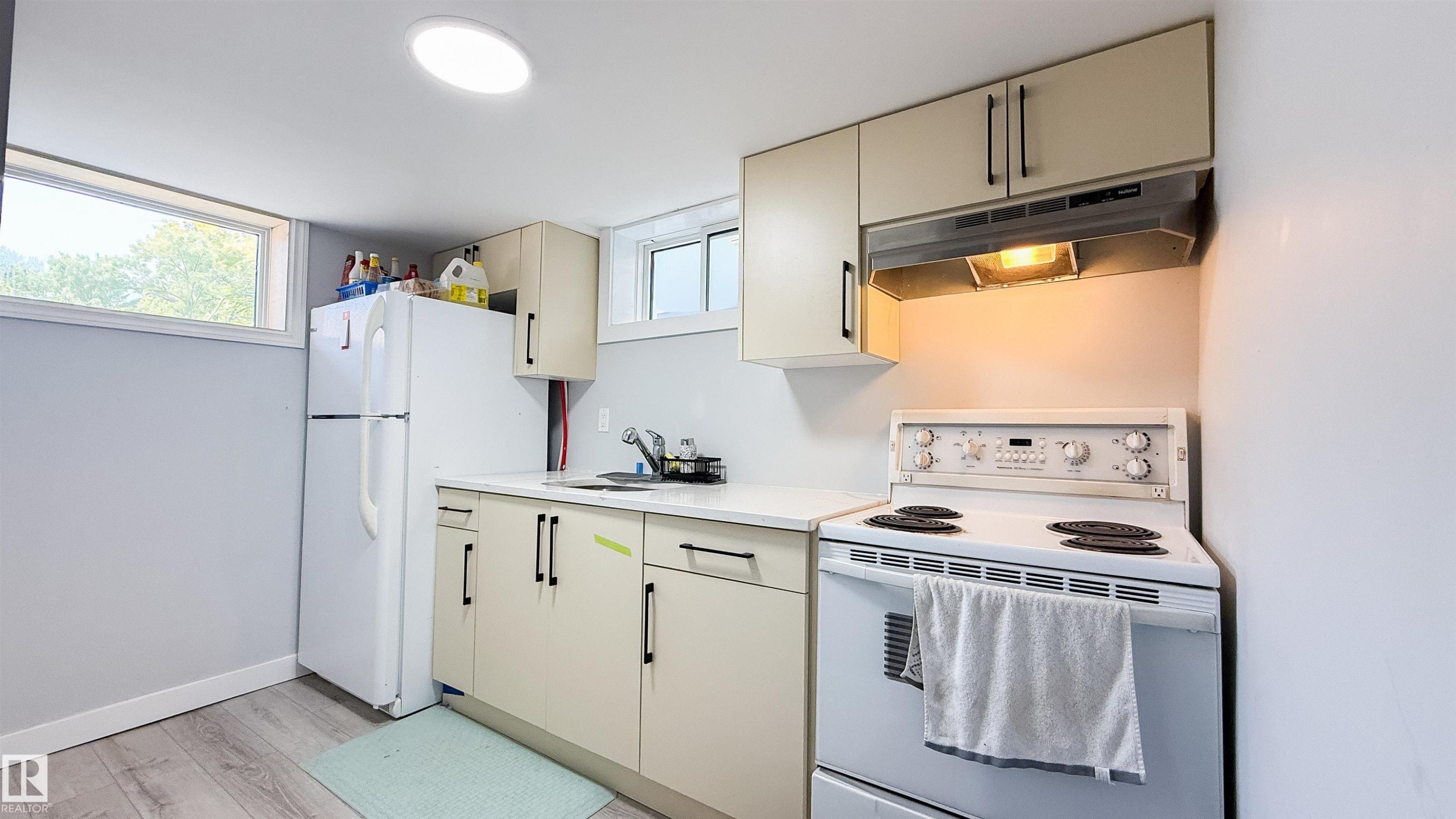 Compact kitchen area featuring neutral cabinetry, a white refrigerator, a white electric range, and a stainless steel sink - 12005 40 St Nw, Edmonton, AB - Indoor Photo Showing Kitchen
