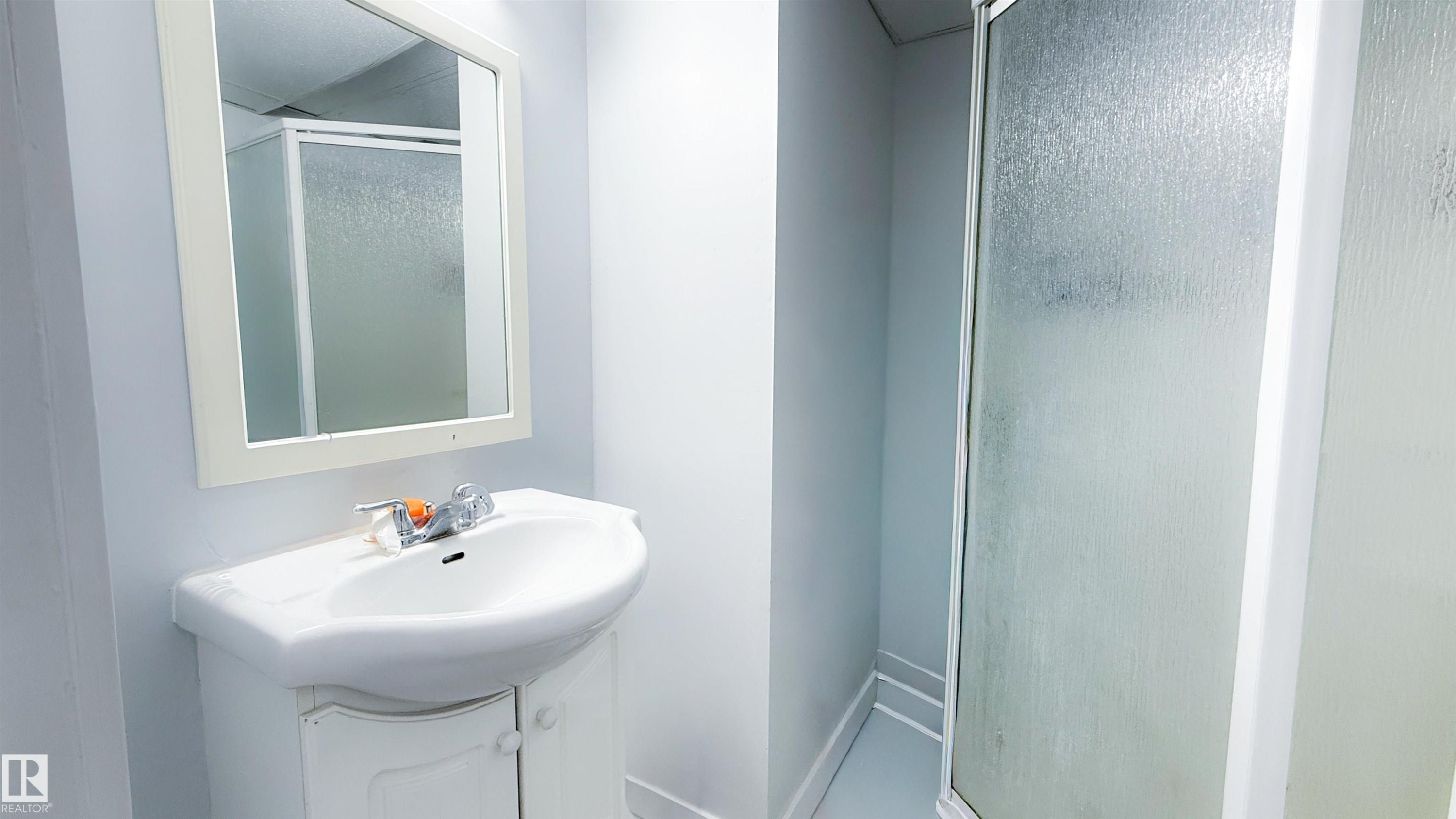 Bathroom featuring a white vanity with an integrated sink, a rectangular framed mirror, and a shower enclosure with frosted glass - 12005 40 St Nw, Edmonton, AB - Indoor Photo Showing Bathroom