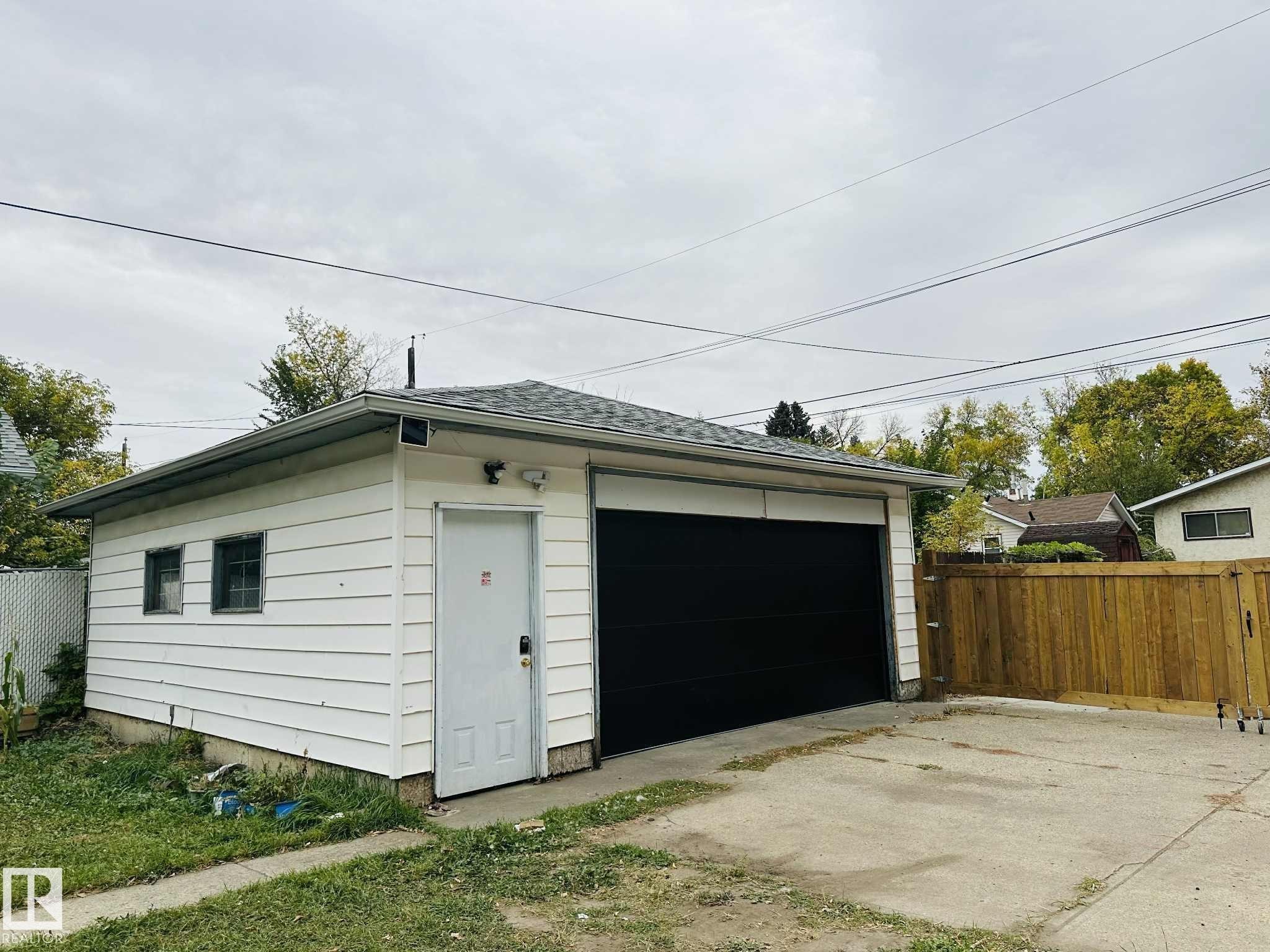 Detached garage featuring white siding, a dark asphalt shingle roof, and a large black garage door - 12005 40 St Nw, Edmonton, AB - Outdoor With Exterior