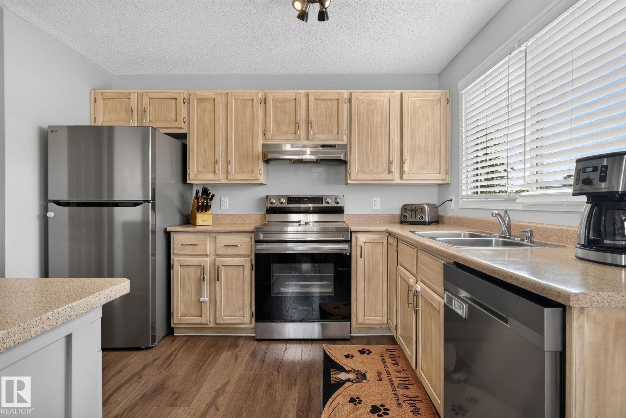Kitchen featuring wood-finish flooring, light-toned cabinetry, stainless steel appliances, a double basin sink, and ample countertop space - 3218 41 Street, Leduc, AB