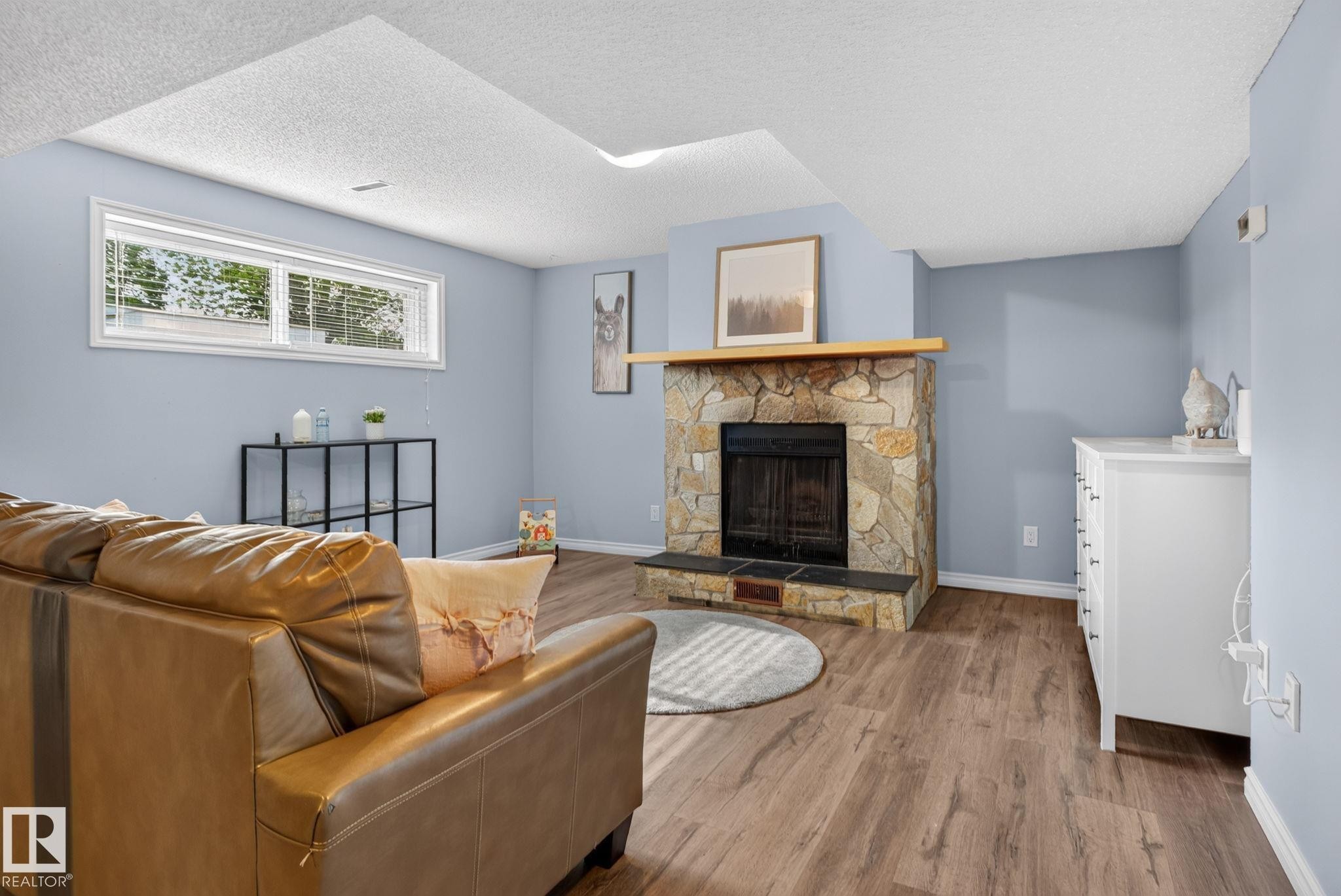 Living area featuring a stone-clad fireplace with a wood mantel, wood-finish flooring, and light blue walls - 3218 41 Street, Leduc, AB
