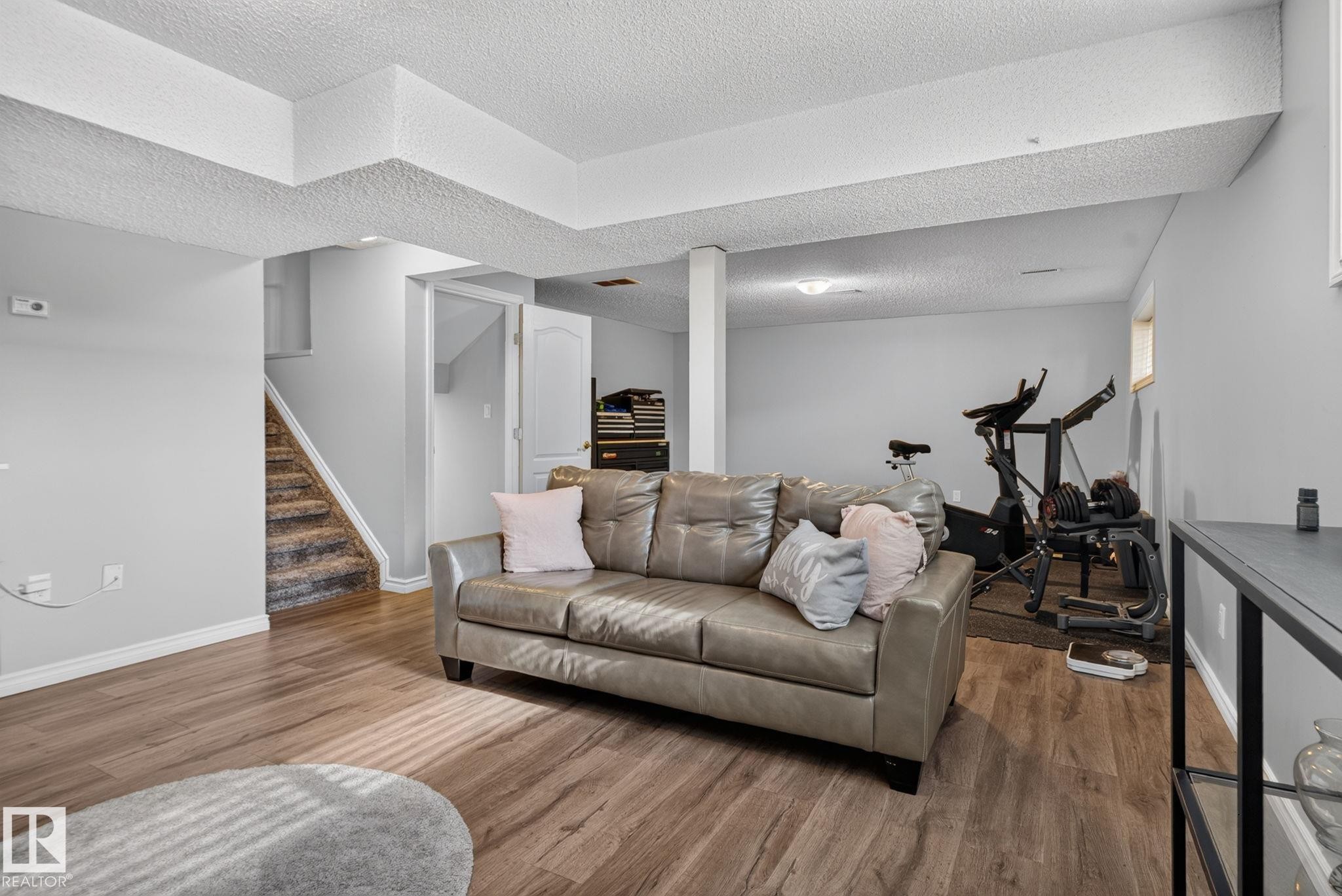 Finished lower level featuring wood-finish flooring, light gray wall paint, white trim, and a carpeted staircase - 3218 41 Street, Leduc, AB
