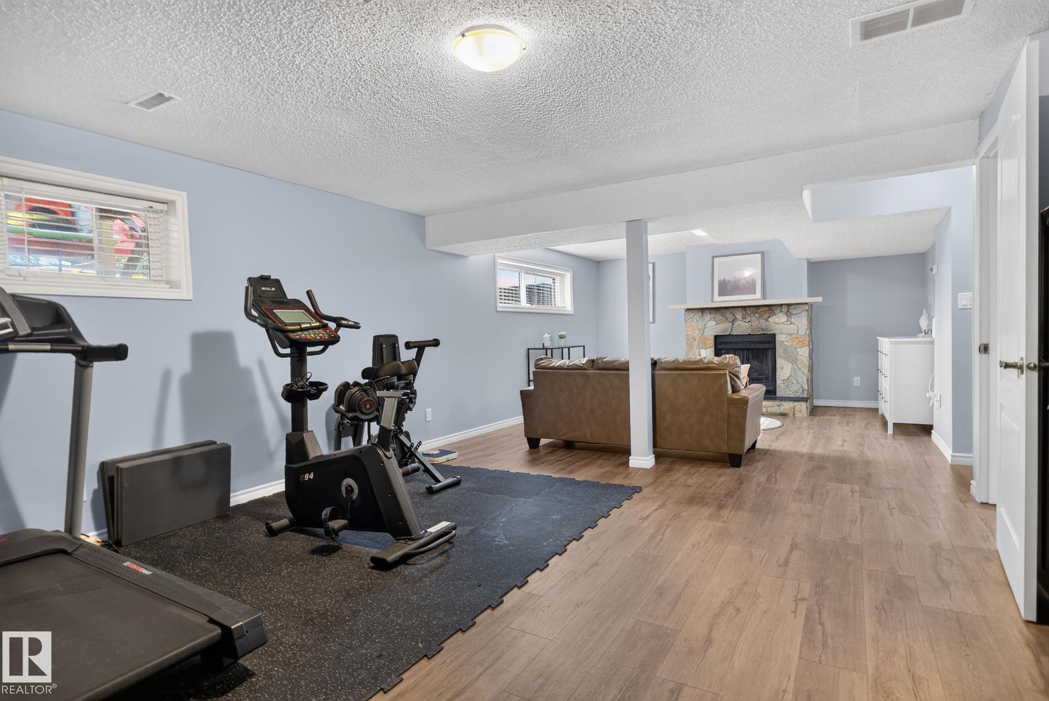 Versatile lower level featuring wood-finish flooring, light blue walls, and a recessed fireplace with a natural stone surround - 3218 41 Street, Leduc, AB