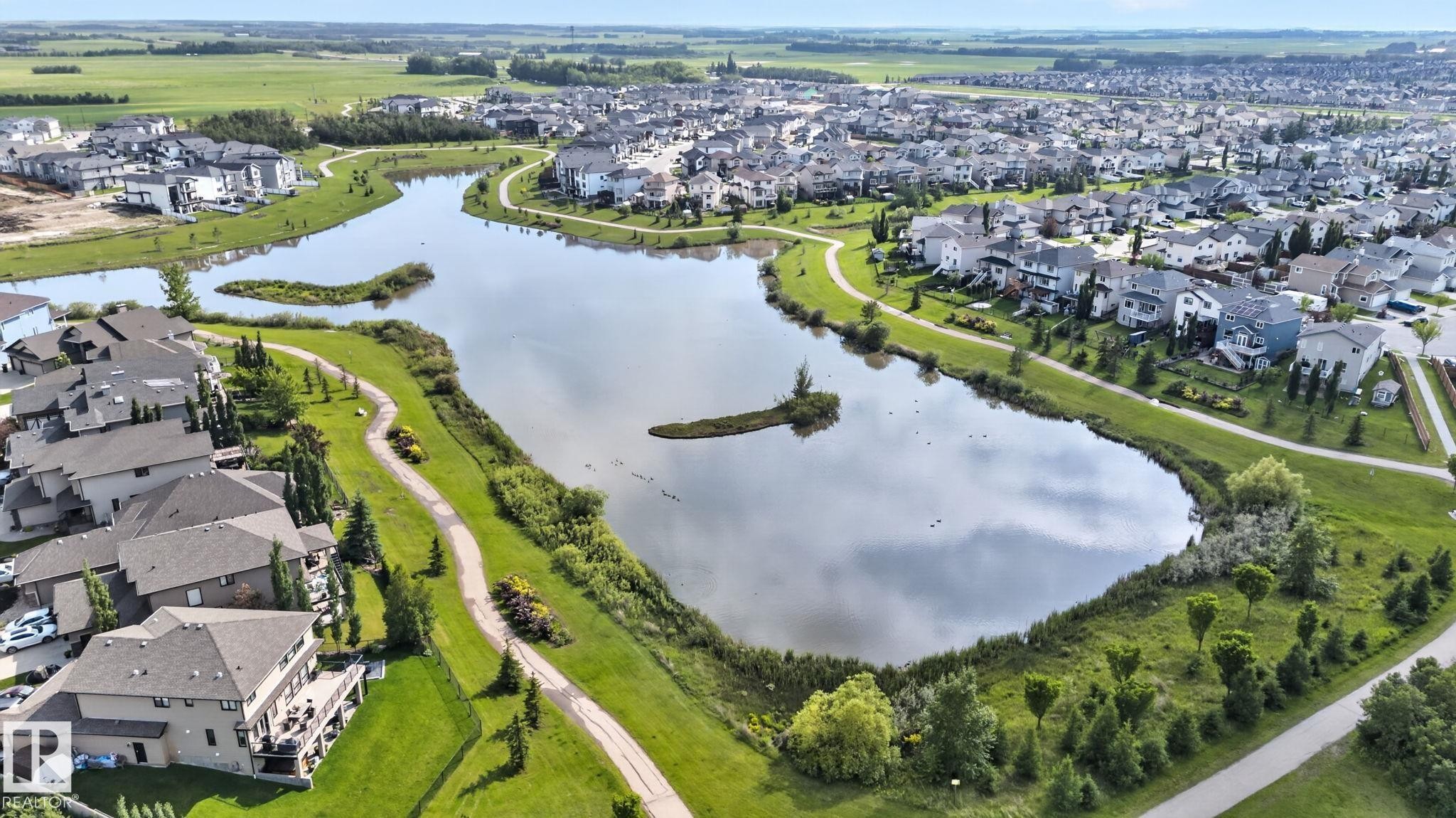 Expansive residential community with a central lake featuring a walking path, mature landscaping, and numerous properties with private decks - 3218 41 Street, Leduc, AB