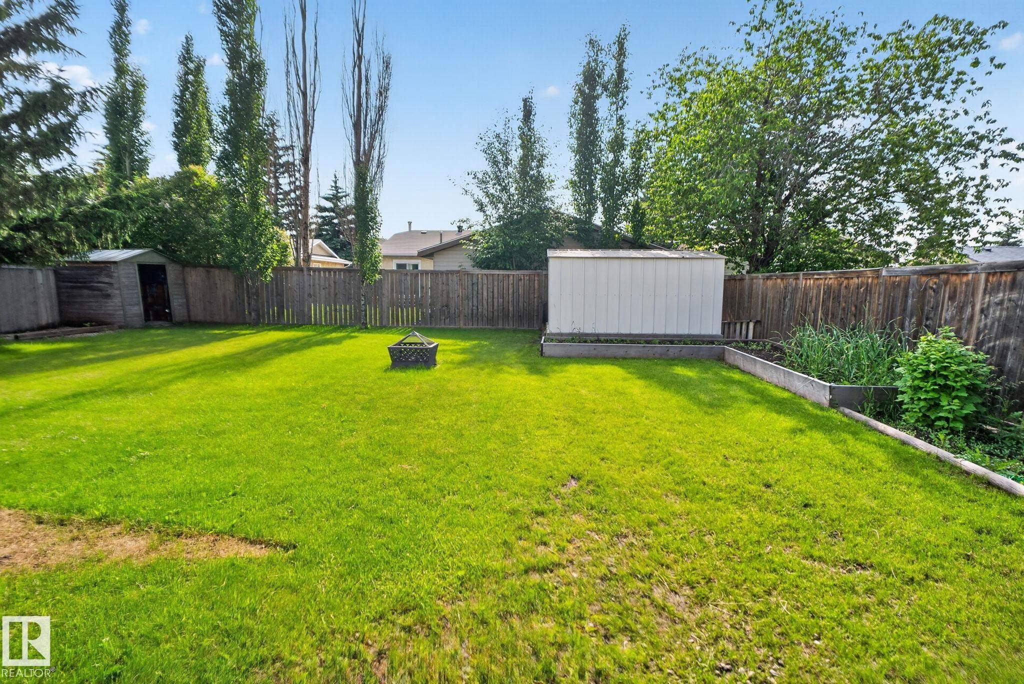 Spacious backyard featuring a manicured lawn, wood privacy fencing, and mature trees - 3218 41 Street, Leduc, AB