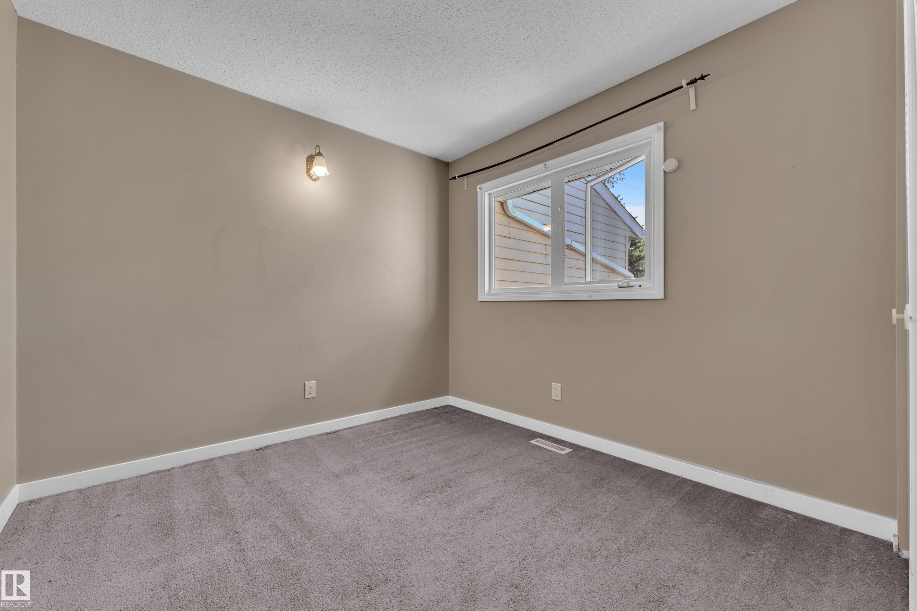 Windowed room featuring wall-mounted lighting, neutral wall paint, white baseboards, and textured carpeting - 6632 36A Avenue, Edmonton, AB